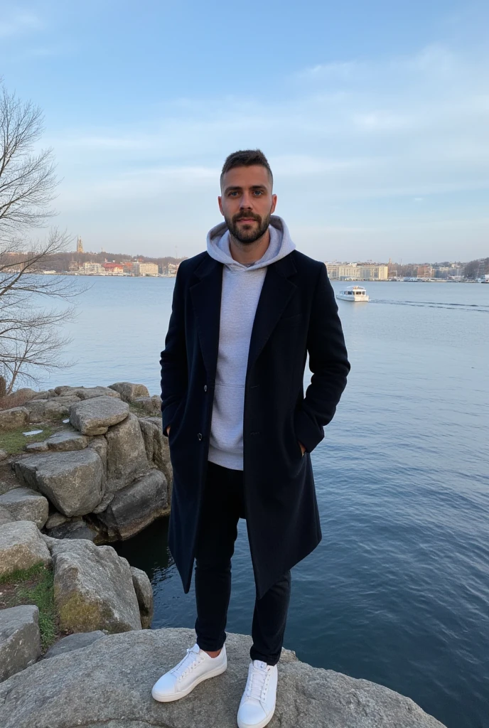 A young man have a light skin tone, a neatly trimmed beard and mustache, with short, dark hair styled short on the sides and longer on top. and a subtle, natural smile that suggests he is enjoying the moment, stands on a rugged cliff overlooking a tranquil bay in Söderström, Stockholm. The scene captures a crisp winter morning with icy blue skies streaked by soft, wispy clouds. The man wears a long black coat with neatly buttoned lapels and white sneakers. His vintage grey hoodie on his head is a deep grey colour, with a soft and casual fabric that appears cosy and well-fitted. The hood is pulled up over his head, framing his face gently and slightly overlapping the lapels of his long black coat. The distant cityscape across the bay glimmers with sunlight, showcasing a harmonious mix of modern towers and classic Nordic architecture. A solitary boat glides smoothly across the water, leaving a delicate wake. Bare, leafless trees and patches of moss on the rocky outcrop add an organic texture, enhancing the serene, introspective mood of the moment. (masterpiece), (best quality), (ultra-detailed background), detailed face, perfect composition, intricate details