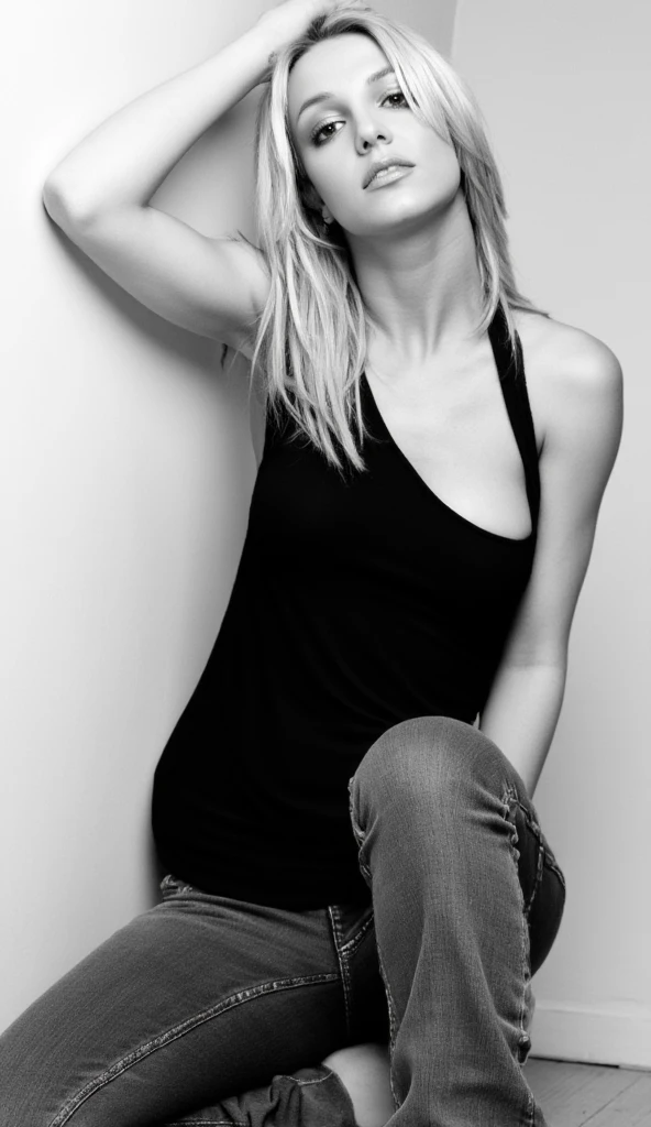 A black-and-white portrait of Britney Spears, seated in a relaxed pose,  with flowing, slightly tousled blonde hair,  a close-up, almost intimate view showcasing her fashion-forward outfit—a simple black sleeveless tank top and a pair of lightly distressed or faded dark wash jeans, mimicking the classic style of a  1990s or 2000s pop idol photoshoot, emphasizing a natural, slightly dramatic light and shadow in a low-key studio setting, using a shallow depth of field,  with a portrait-style lens accentuating her facial features,  captured in a medium shot, with a slightly high-angle viewpoint,  creating elegant and effortless poses and expressions, reminiscent of a polished, high-fashion magazine spread shot from a soft-focused lens, emphasizing the natural curves of the model's body, with an overcast or diffused, slightly muted light to achieve a classic, timeless aesthetic using 2000s photo tones,  reflecting the era's iconic music video style. britney.