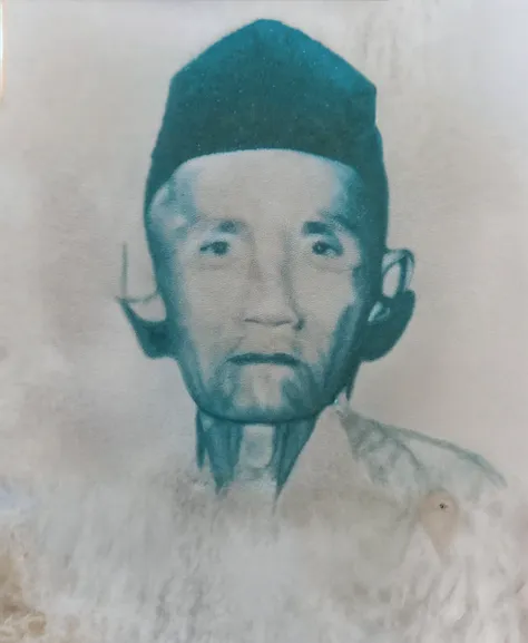 Indonesian Muslim male, measuring 45 years or above, wrinkled brown skin, wearing small transparent glasses, blue head covering, wearing old Islamic clothes, oval face, slightly narrow eyes, not too thick lips, has a beard, and thin mustache, HD realistic picture