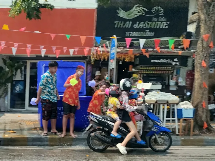 A handsome young Thai teenager,Wear boxer shorts and no shirt to ride a motorcycle.,Holding a water gun at the Songkran Festival in Bangkok,Flour smeared,There was a person walking behind him holding a water gun.