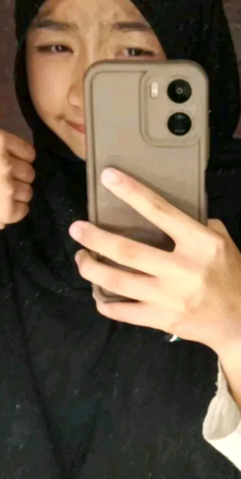 A guy and a girl, a guy holding a girl in his arms, holding her hips, he is wearing black pants and a black T-shirt, he has dark hair that is wavy. The girl is sitting in his arms, hugging him with one hand around his neck, she is wearing a gray hoodie and gray pants, with the other hand she is holding a phone and taking pictures of them both in the mirror, the girl's face and hair are not visible, since she has a hood from a gray hoodie on her head. In the background there are black walls and panoramic windows with a view from Moscow City to the city highway with many cars in the distance.