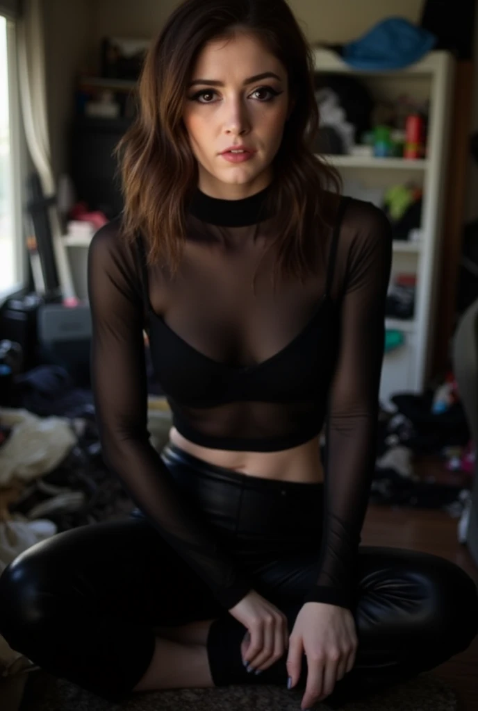 a photograph of Chrissy Costanza in a messy bedroom wearing a wearing a sheer, long-sleeve black top that reveals a black bra underneath, and a black leather pants, she is looking straight at the camera, full body image.
