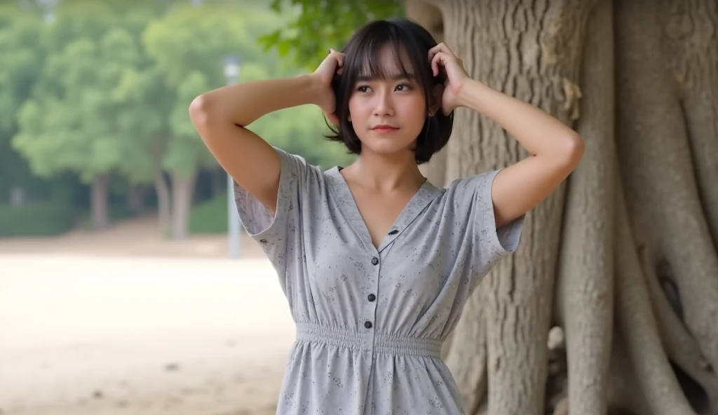 A woman, positioned slightly to the left of center in the image, is seen from mid-thigh up. She has short, dark hair, and is wearing a light-grey, patterned, loose-fitting midi-dress. hands behind her head showing her armpits. The dress has small, patterned dots, and a V-neck. Her expression is neutral or slightly pensive. She is light-skinned with visible facial features, and her posture suggests a casual, relaxed pose. The woman is oriented facing the camera. The background is out-of-focus, with a light-grey/beige area suggesting a beach or park. A large tree trunk, with a rough, light-brown, and grey bark, is visible on the right side of the image, providing depth and a natural backdrop. The lighting is soft and diffused, casting no harsh shadows. The overall style is casual and serene, with a natural, outdoors setting. The image's color palette is soft and light, with a predominance of greys, light browns, and beiges. The composition is balanced, with the subject's position drawing attention, while the background provides a natural and calming ambiance.