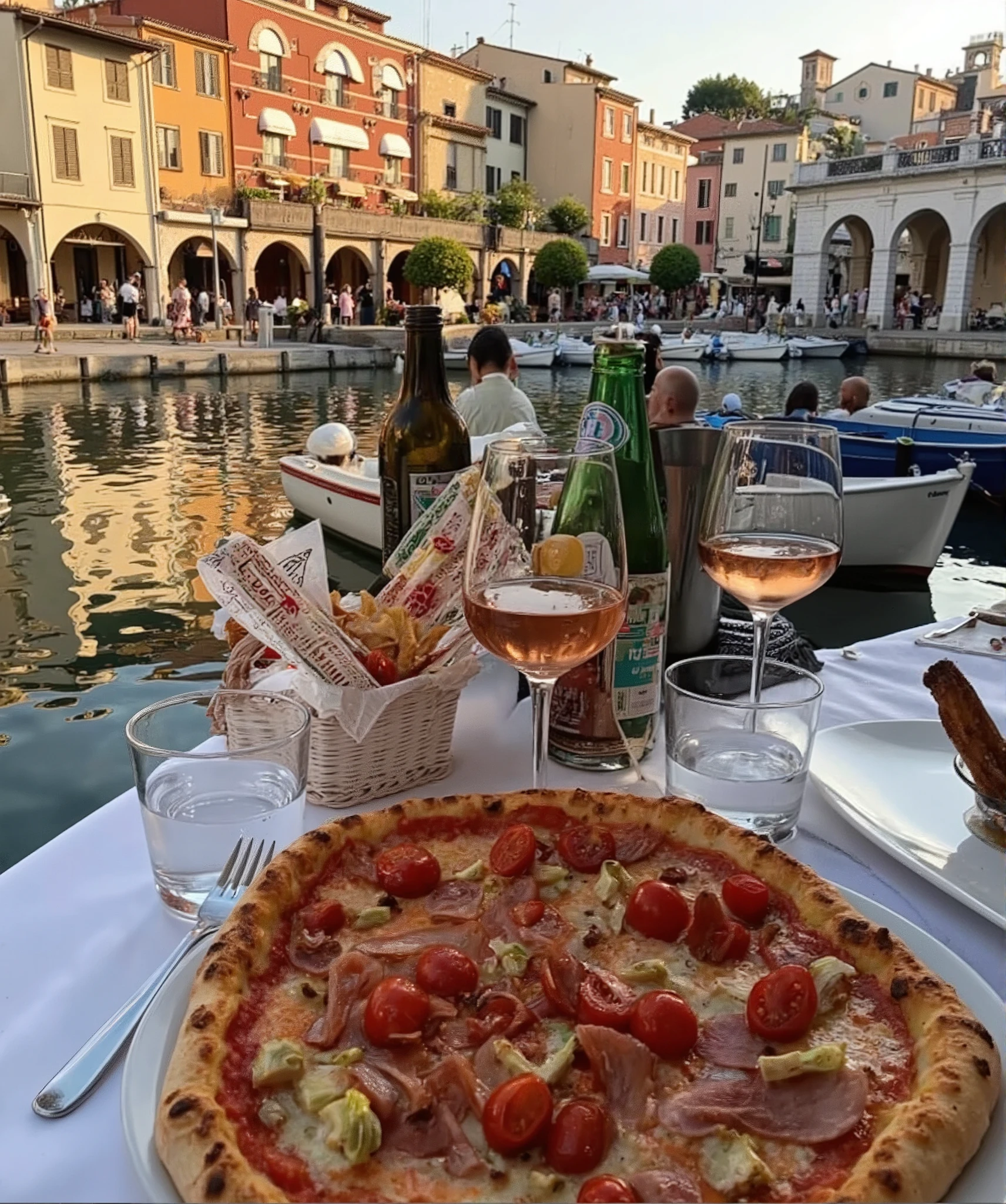 /imagine prompt: a picturesque outdoor Italian dining scene by a waterfront with colorful historic buildings and boats docked nearby. The table is elegantly set with a delicious pizza topped with cherry tomatoes, artichokes, and slices of cured meat. There are glasses of rosé wine, sparkling water, and a basket of Italian breadsticks. The sunlight bathes the scene in a warm golden glow, reflecting on the water. In the background, people are leisurely walking under arched porticos, adding a lively yet relaxed atmosphere. --v 5 --ar 16:9 --style cinematic --q 2 --hd