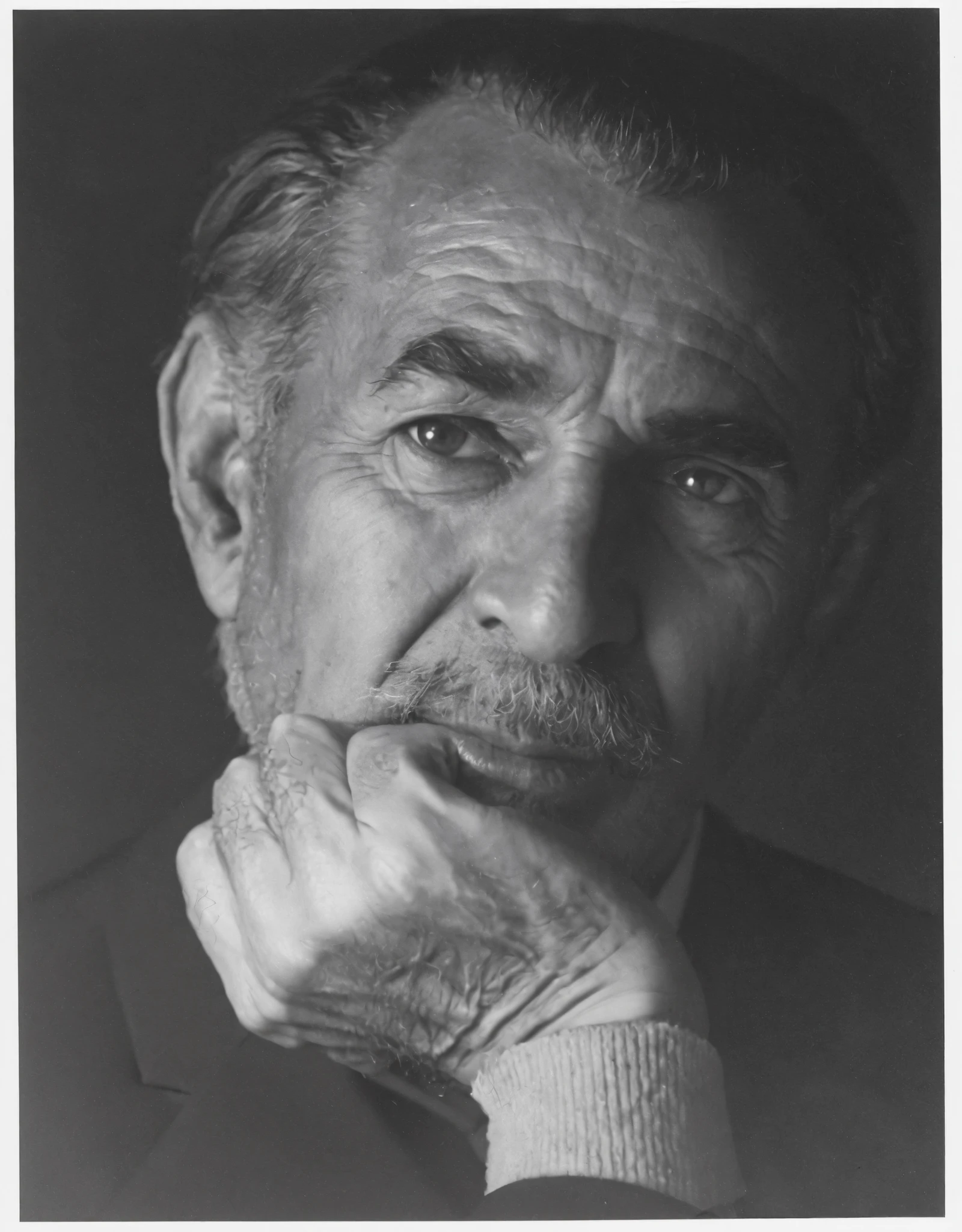 A highly detailed, black-and-white portrait of an elderly Egyptian architect, Hassan Fathy, in black suit His face is deeply expressive, with wrinkles showing wisdom and experience. He has neatly combed back hair, a mustache, and slightly squinting eyes reflecting contemplation. The lighting is dramatic, with soft shadows adding depth to his facial features. The background is blurred, showcasing traditional Middle Eastern architecture, with textured walls and intricate woodwork. The image is inspired by vintage photography from the mid-20th century, with a film-like grainy texture and artistic composition. The mood is thoughtful, intellectual, and timeless. and in black and withe monochrome