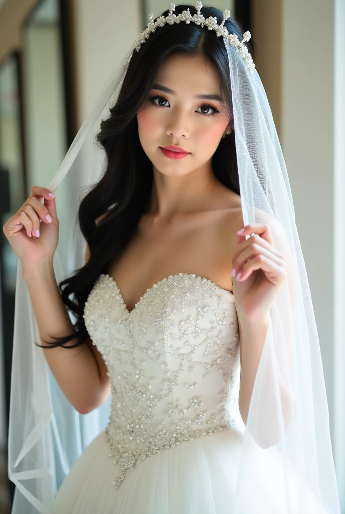 The image showcases a beautiful young woman dressed as a bride. She wears an elegant white wedding gown adorned with intricate floral embellishments and shimmering sequins. The dress features an off-the-shoulder design, accentuating her delicate shoulders and décolletage. Her long, dark hair cascades gracefully, partially covered by a sheer, flowing veil. She holds the edges of the veil with both hands, lifting it slightly as she gazes softly into the camera with a serene and enchanting expression. The background includes mirrors and soft, neutral tones, adding depth and elegance to the scene. The lighting is gentle and diffused, enhancing the dreamy, romantic atmosphere of the photograph.

