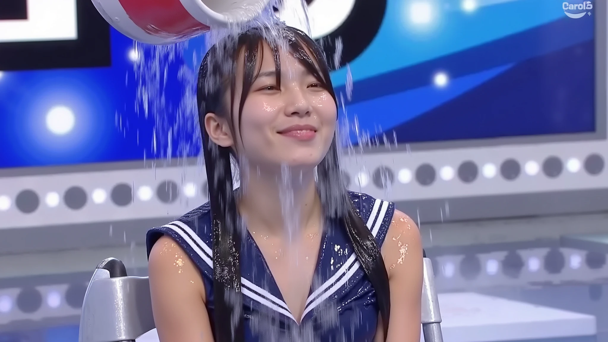 On a TV gameshow, a beautiful young 21-year-old Japanese woman with twintails and wearing a dark blue sailor suit sits in a folding chair on stage as a bucket of water is poured over her head from off-screen. She looks up into the path of the water, so the water lands in her face, rather than on the top of her head. She is absolutely soaked and her hair is all straggly. Photorealistic.