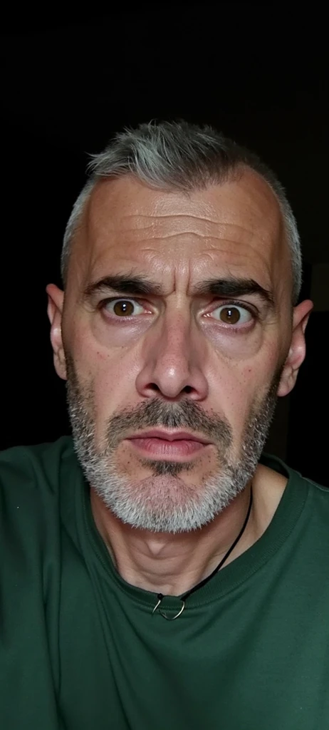 The image is a close-up of Cristiano Ronaldo face. He appears to be in his late 40s or early 50s, with a bald head and a goatee. He is wearing a black hoodie and has a serious expression on his face. His eyes are wide open and his mouth is slightly open, as if he is making a silly face. In the background, there is a bedroom with a bed, a nightstand, and a window with red and white striped curtains. On the wall, there are several framed pictures of a muscular man.