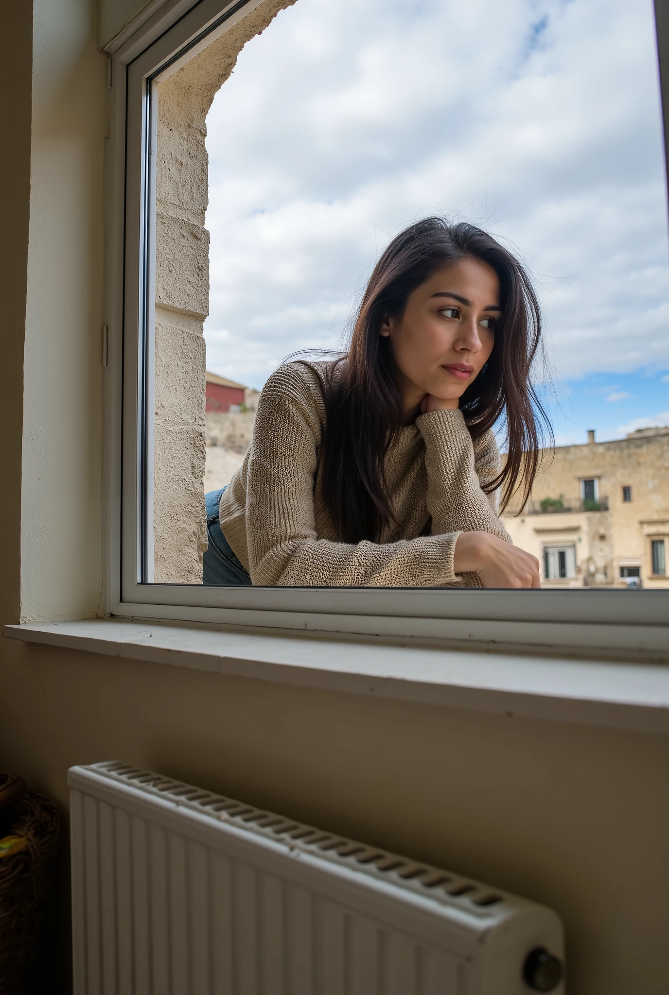 Photo from indoor. extreme low angle view of a window in a house in Sassi di Matera. A woman (50% russian, 50% nigerian) looking out the window. Elbows on the windowsill, view from behind, long dark brown hair, a beige cotton sweater, she wears jeans. She sighs wistfully. The shot frames a house outside the window. Framing of the house outside.Photographic shot, lens flare and backlit effect. Clear cloudy sky