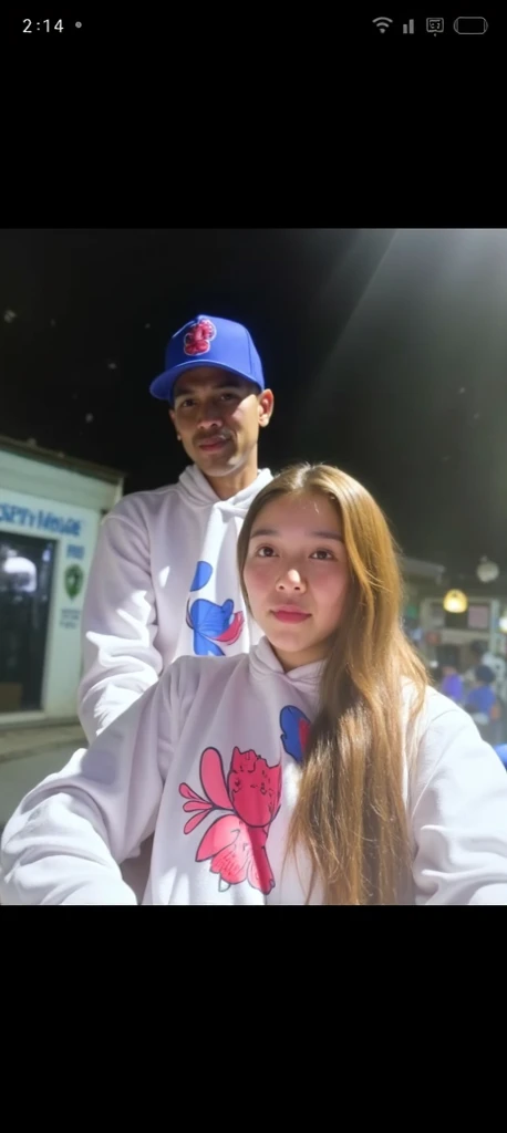 A couple, the woman is from Indonesia and the man is from Canada. The man is chubby and the woman is slightly plump. Holding each other and smiling, the woman wears a beige hijab, white blouse and beige skirt and the man wears a white t-shirt and short beige pants, has a beard and thin mustache and wears a beige beanie.