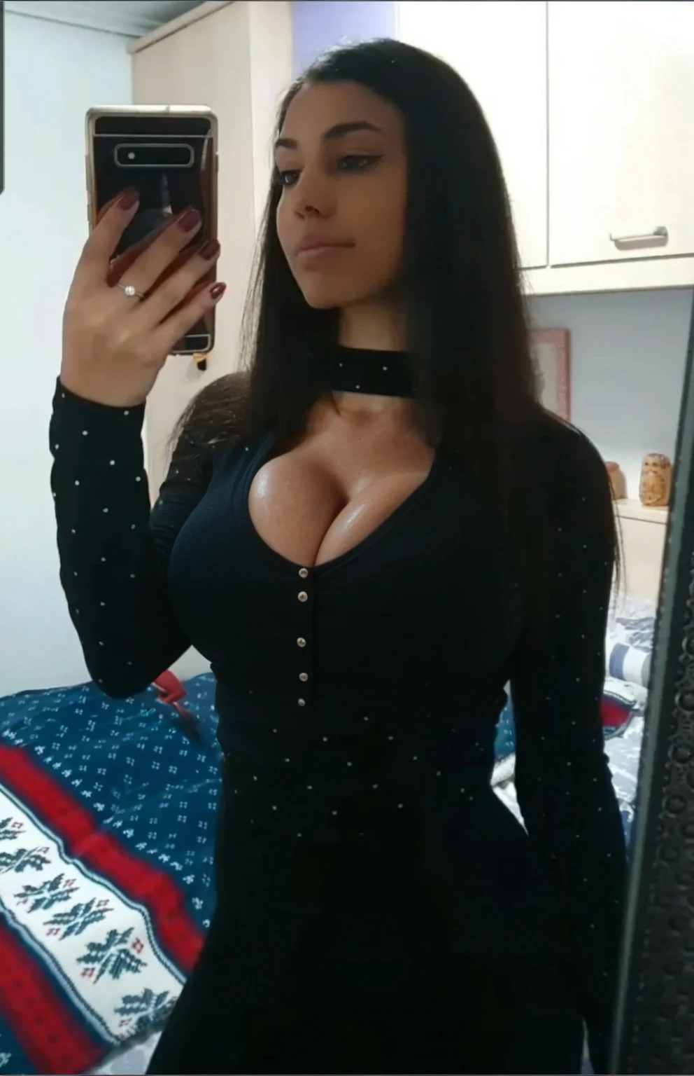 A white woman with black hair and large, voluminous breasts showing through a low-cut black blouse with a large nude neckline showing