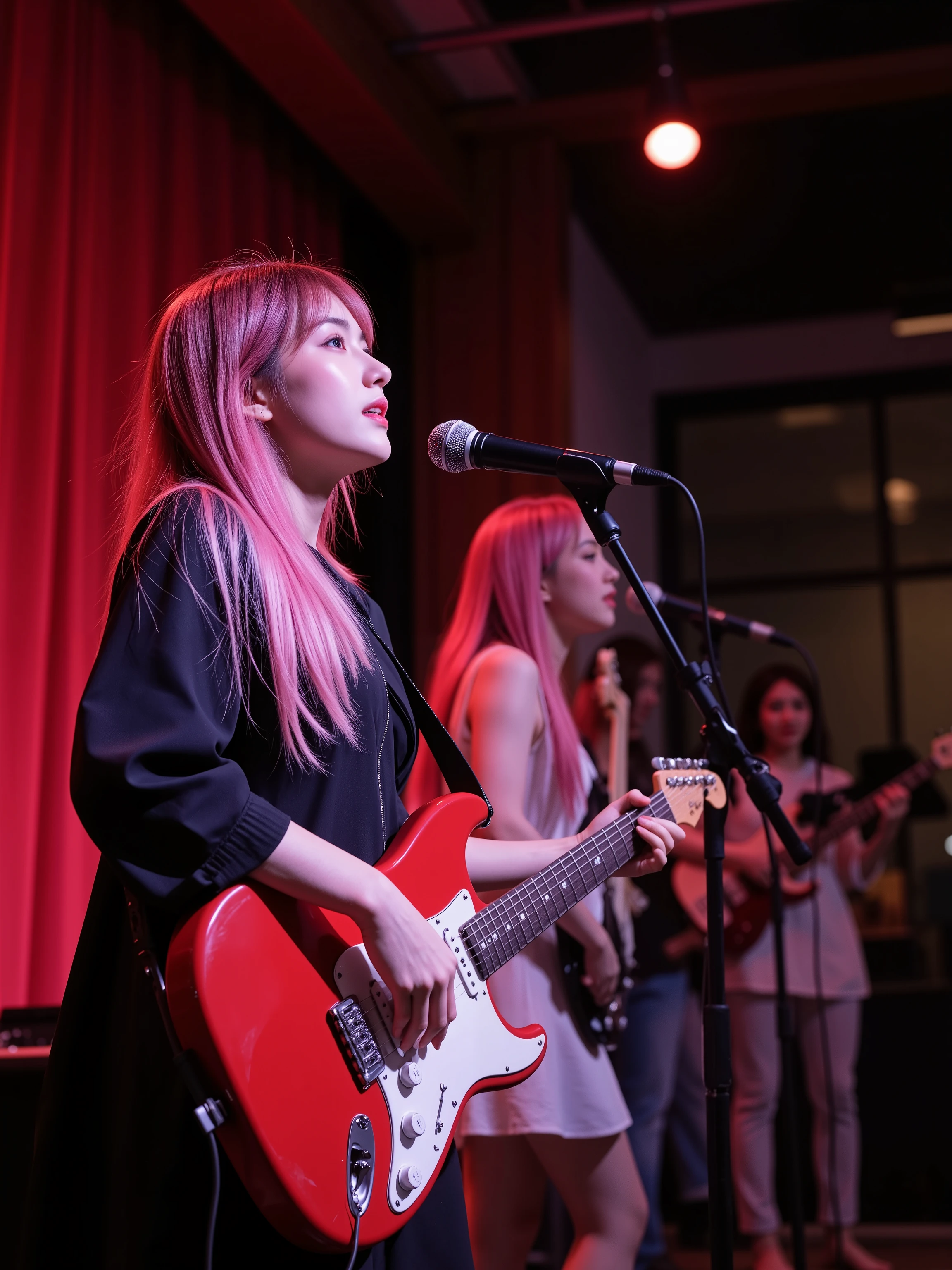 On the stage of a small live music club, a young cute Japanese woman in a gothic-ta outfit with her hair up plays electric guitar, while a cute Japanese beauty with long pink hair and white ta fashion plays bass guitar while they both smile and sing loudly.