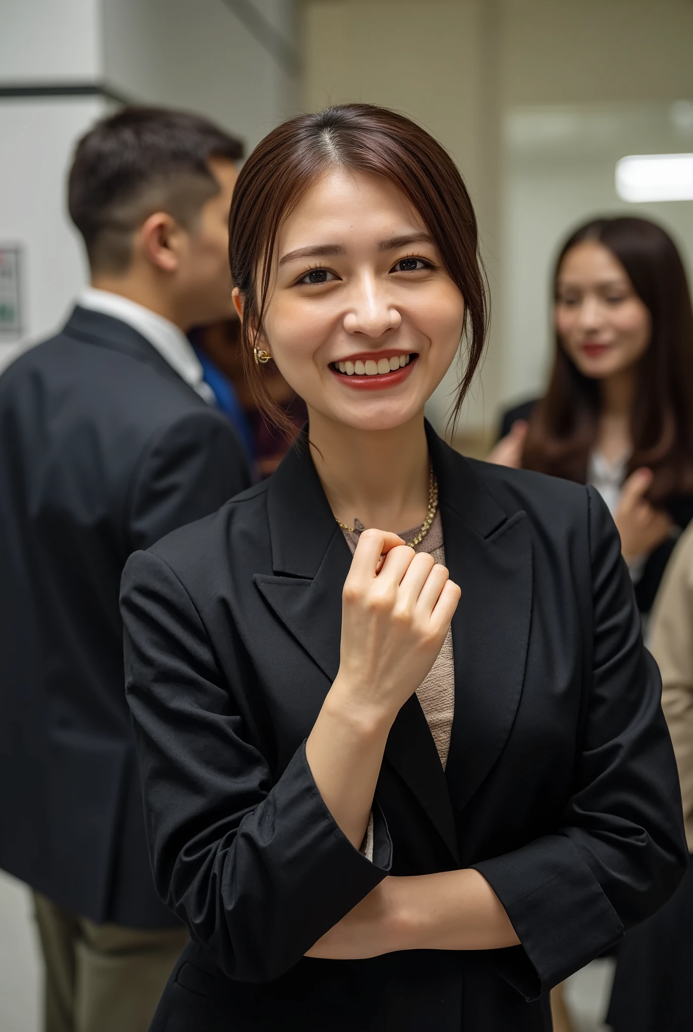 Neat Young Woman、and look at the camera、office lady suit、jacket、shirt、necklace、ear piercing、smile showing teeth、people talking in the background is inside the room、
