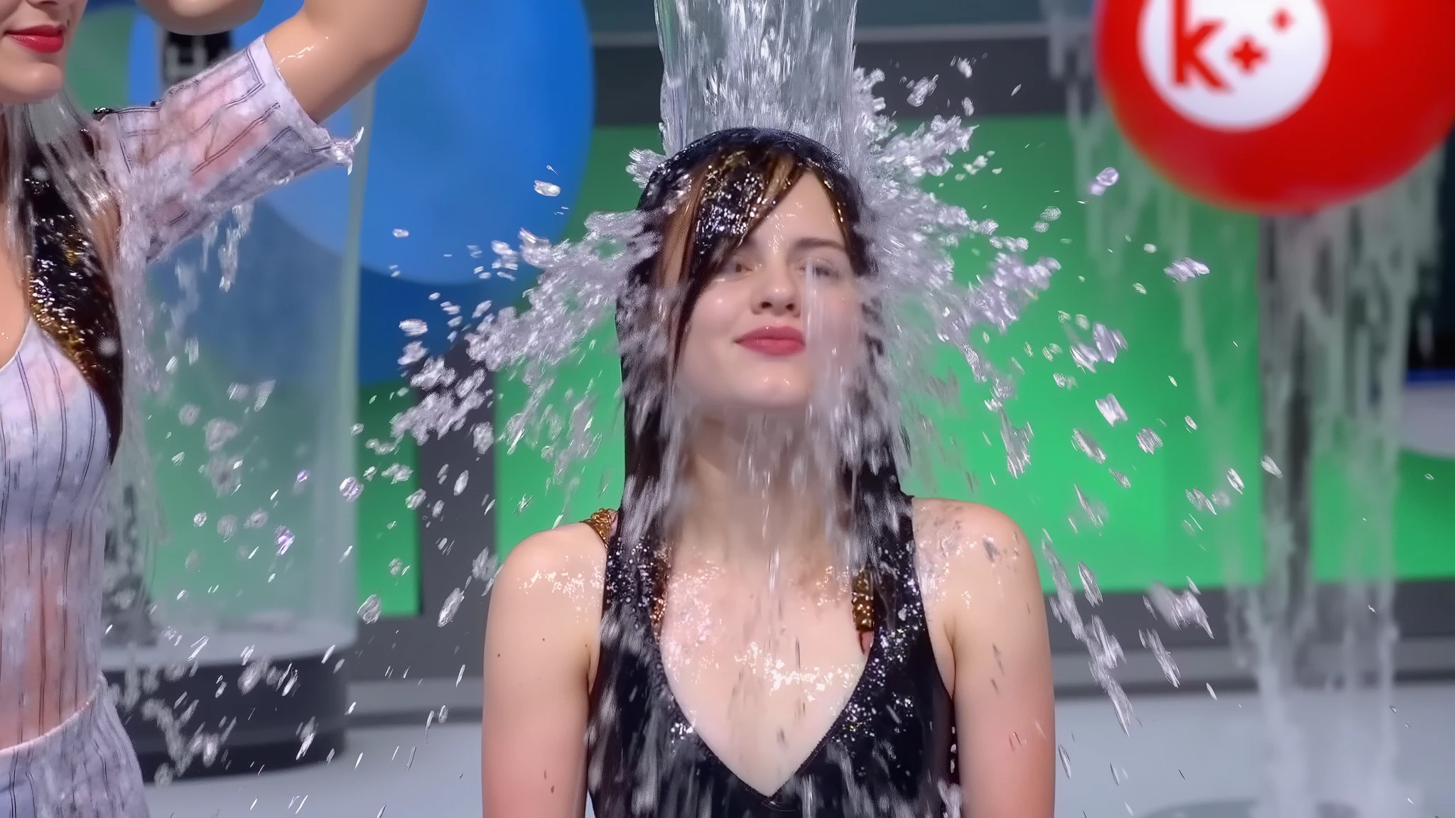 On the set of a TV gameshow that is elaborately decorated with lots of set dressing and brightly lit with lots of coloured lights, a beautiful 18-year-old Japanese girl with black hair in twintails, wearing a maid outfit, jewellery, lipstick and makeup has a bucket of water poured over her head by the show's hostess, who is wearing a dress. The water runs down the girl's face and completely soaks her. Photorealistic. Close-up. Headshot. 1girl. Solo.