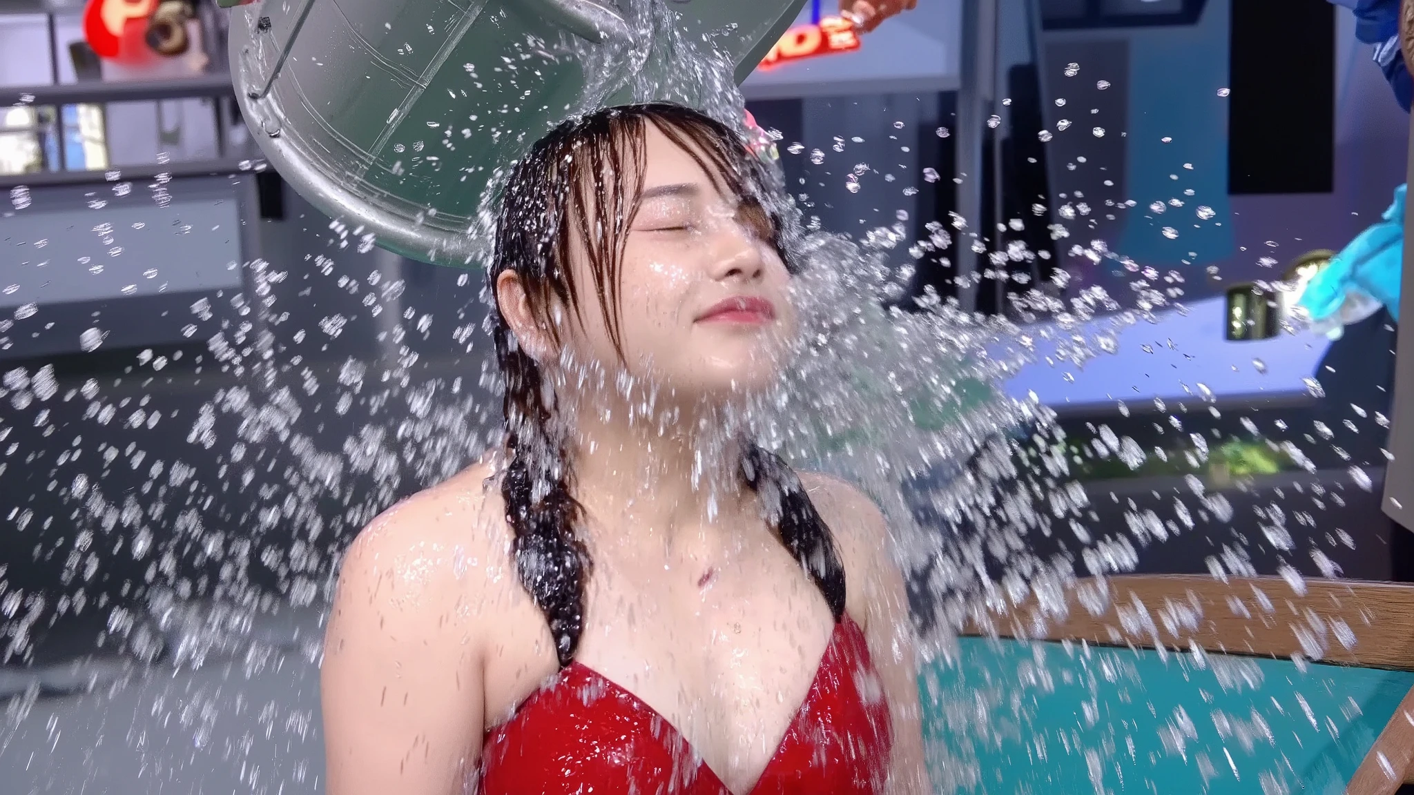 On the set of a TV gameshow that is elaborately decorated with lots of set dressing and brightly lit with lots of coloured lights, a beautiful 18-year-old Japanese girl wearing a brightly coloured formal dress, jewellery, lipstick, eye shadow and long press-on false nails has a bucket of water poured over her head by the show's hostess, who is wearing a dress. The water runs down the girl's face and completely soaks her. Photorealistic. Close-up. Headshot. 1girl. Solo.