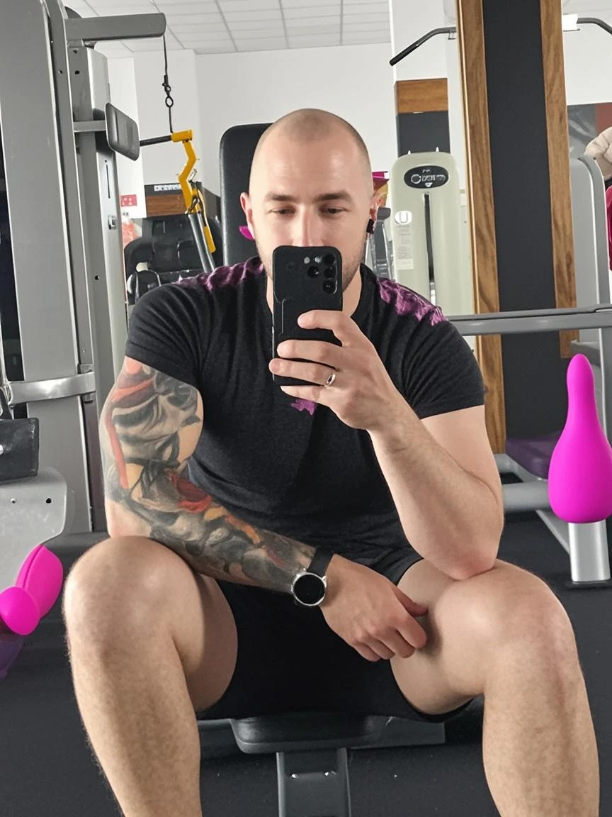 there is a man sitting on a step with i phone held by his left hand, fit pic, manly and handsome face, sporty physique, prefect body, squatting down on stairs his legs spread apart, very big pink erect , big chubby pecs, very shiny wet sweaty muscles, musculine stocky wrestler body, big arms, wide shoulders, big chubby thighs, wearing white sneakers, his left hand puts on his left knee, wearing cap on his head, nighclub and bar and streets background, white flawerless shiny wet looking skin