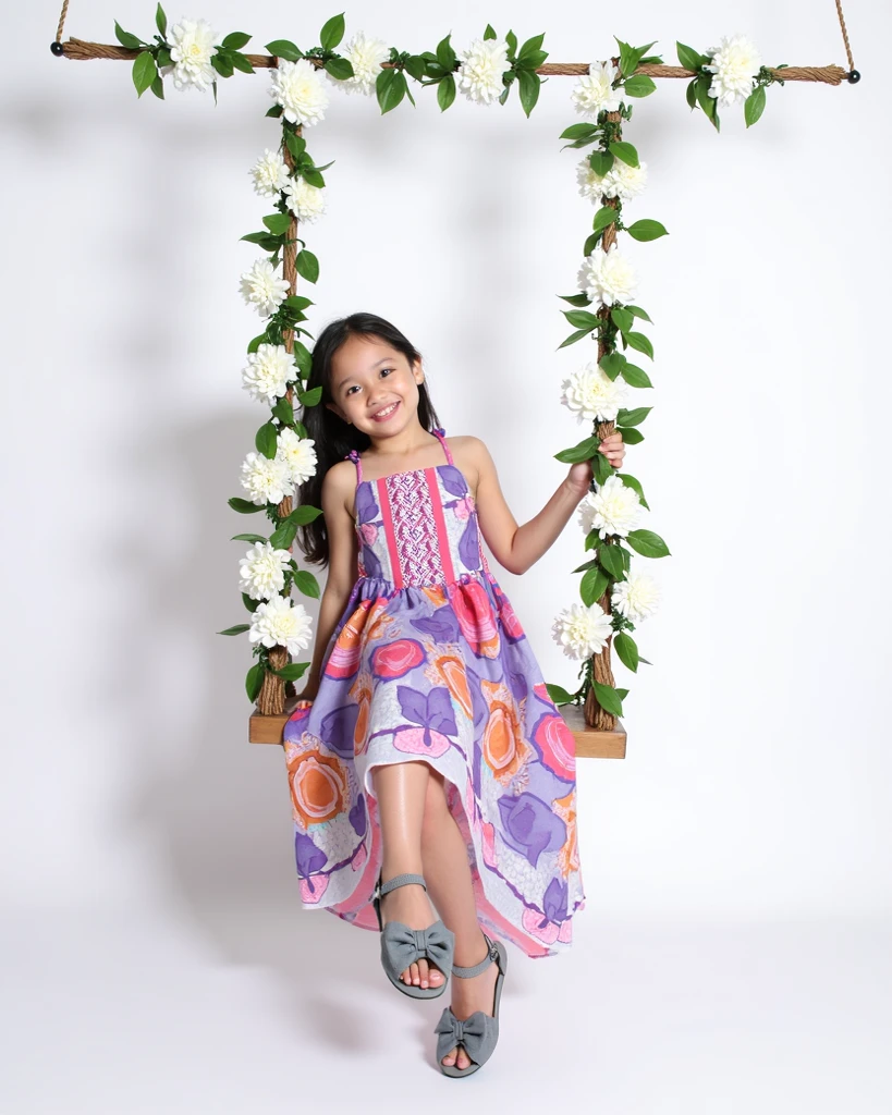 Realistic filipina of 5 year old girl wearing a pink princess dress and looking in camera at the back the girl sitting chair.The background is park of playground.
