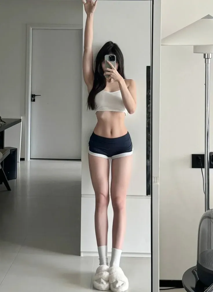 A woman takes a selfie in the mirror, Photos of slim girls, her navel exposed, thin waist, 24 year old female model, thin waist粗臀, Photos of slim girls model, Good butt,Leg length, 19 year old girl, wearing shorts, smallest belly ever, beautiful belly