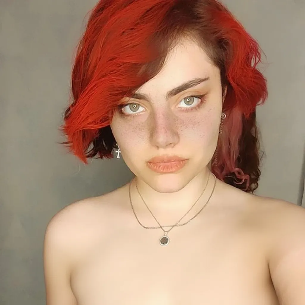 A hot girl with short red hair is lying on the bed in a gray bedroom Red Bra