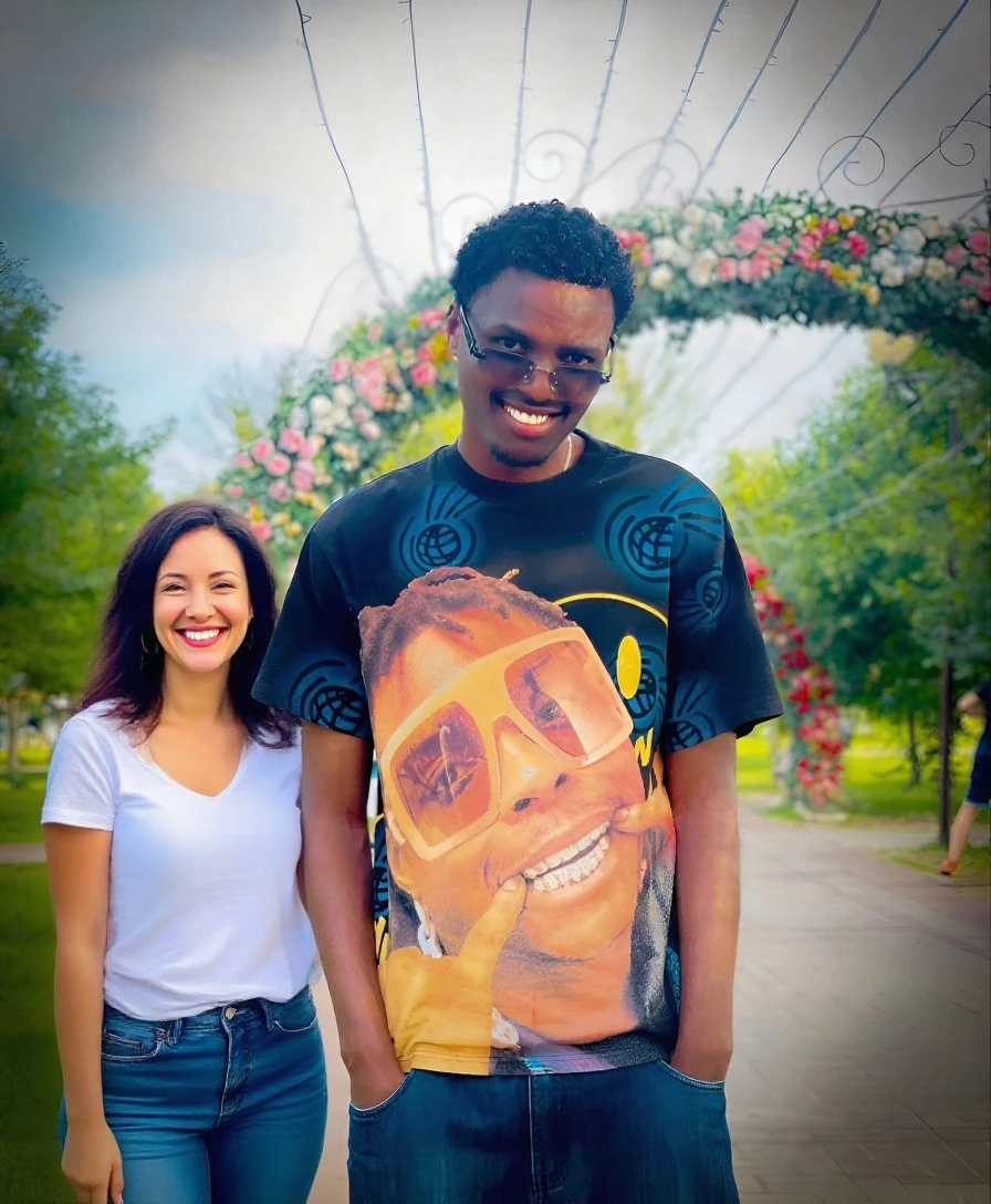 make a picture of a man with curly hair, a bit fat with a tall body and tanned skin, wearing a red T-shirt with writing on it "Educate the Lover" bringing flowers with a beautiful tall woman with a 34f chest wearing lingerie