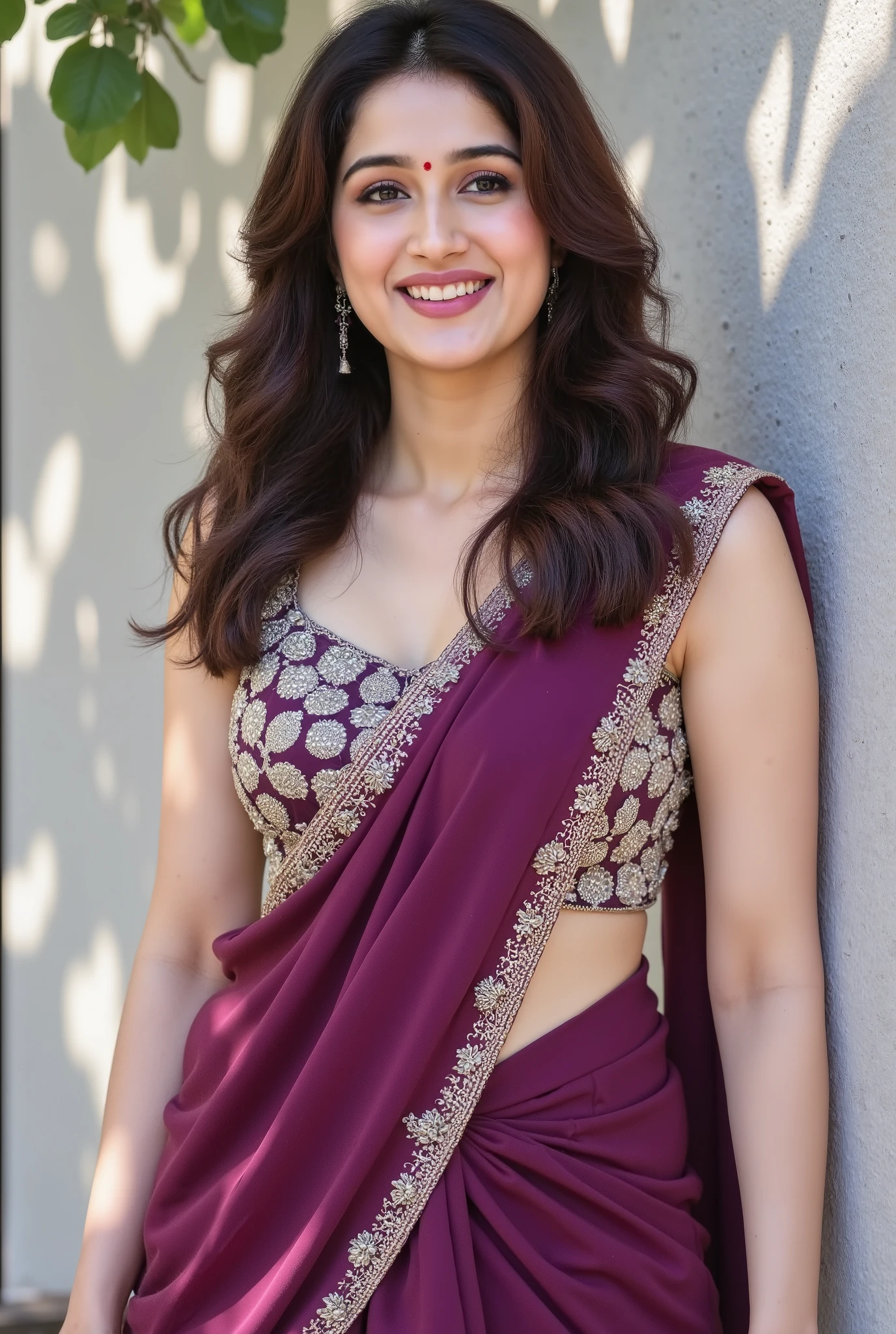 A young woman with long wavy hair smiles warmly while leaning against a textured light grey wall under dappled sunlight and shadow from leaves. She is wearing a deep purple traditional Indian outfit with intricate gold embroidery on the front, and a matching dupatta draped elegantly. Her natural makeup, small bindi, and joyful expression create a serene, candid, and elegant mood. The composition is bright, airy, and minimal, capturing the warmth of a sunlit moment with soft, natural shadows and highlight