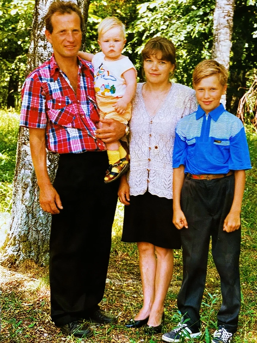 CHILD(male genderno) with green eyes, blond hair, white blouse and cargo pants, Holding a little black dog on his lap , in a wooded park , with green grass