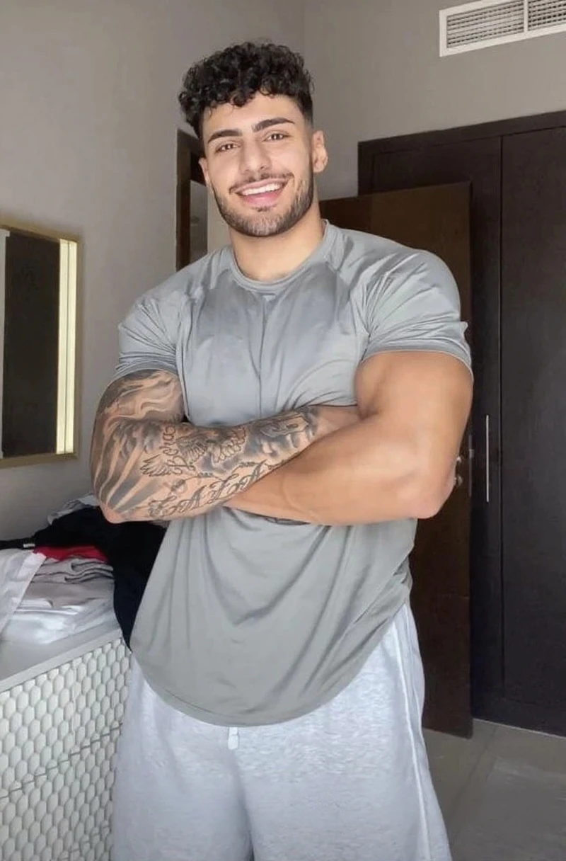 Hombre varonil con barba y ropa elegante parado frente a un edificio, cuerpo musculoso, enfoque en el pectoral, pectorales grandes, pectorales sin vello, cara definida, obra de arte, pelo cepillado, piel morena, dick bulge, daddy, dadbody