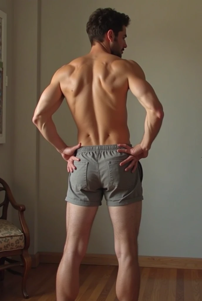 black man with his back to the camera, shirtless and barefoot, wearing gray shorts