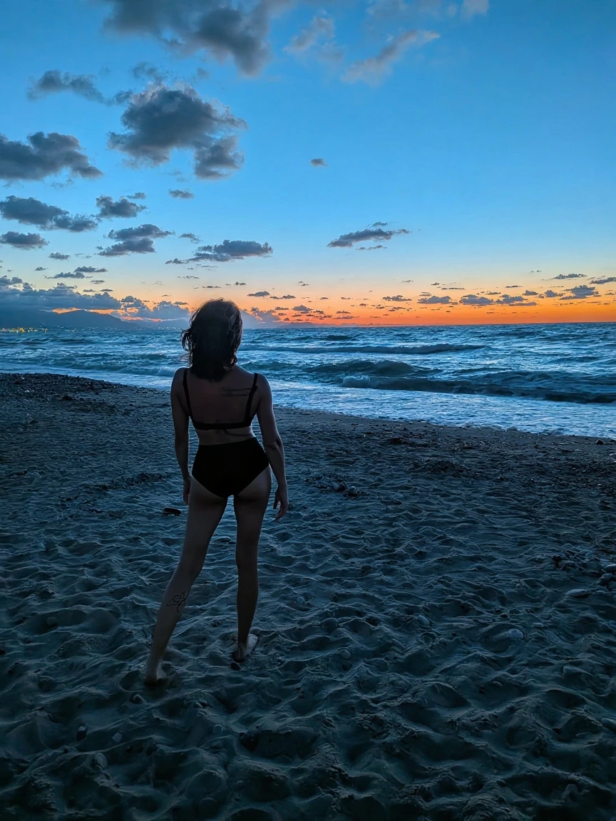 Picture a genuine moment by the shore: As the sun begins to set, casting a warm glow, a young woman, wearing a simple black bikini, runs along the water's edge. The sand, slightly wet from the tide, clings to her feet with each step, leaving behind a series of clear footprints. Seagulls glide overhead, their calls mixing with the rhythmic sound of waves breaking against the shore. Families and couples dot the beach, engaged in their own activities. This scene captures the essence of a typical day at the beach, emphasizing the natural beauty and simplicity of the moment.