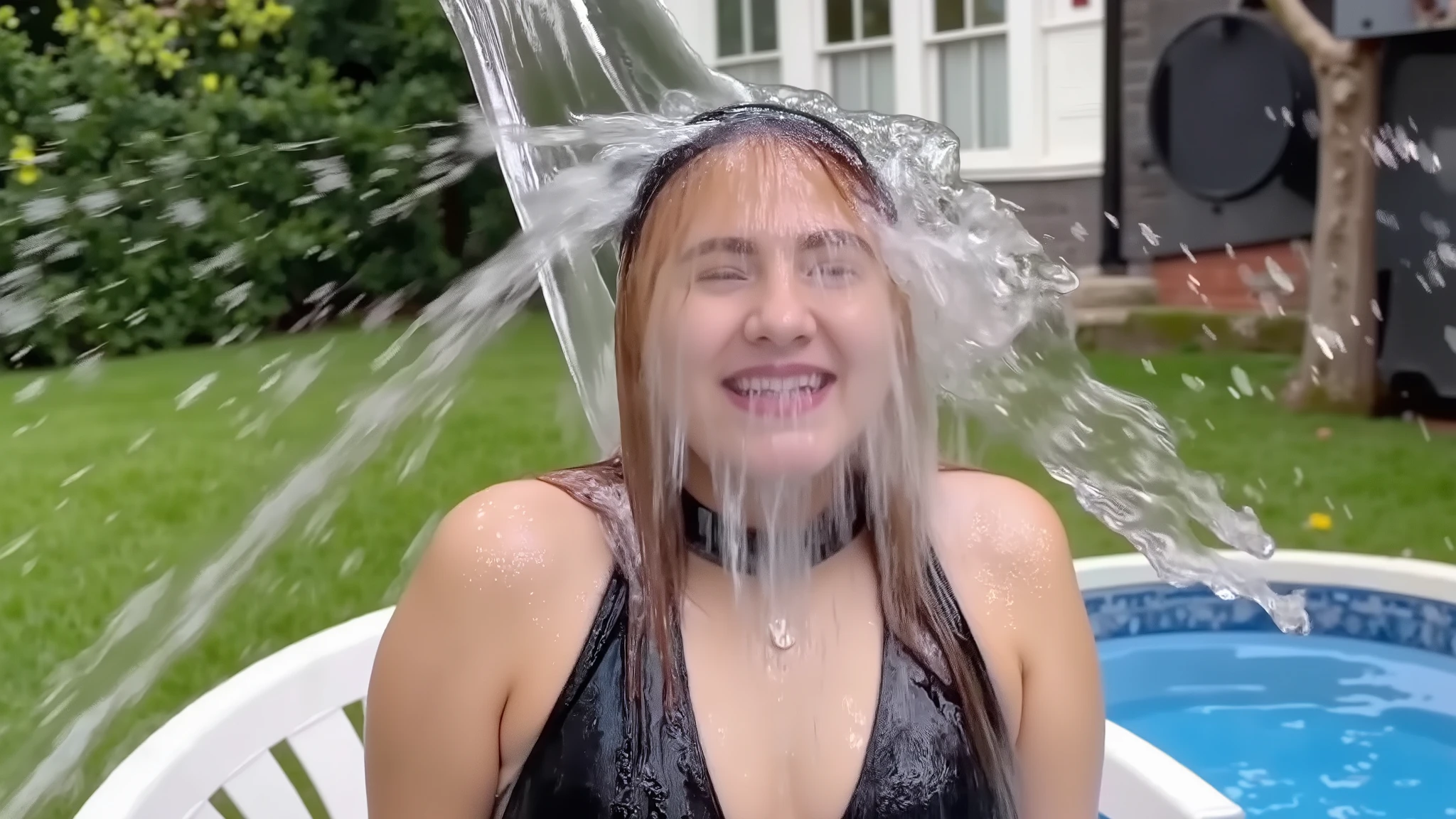 A beautiful young 18-year-old girl with long, pale blonde hair and big breasts. She is wearing a black lace bra, black lattice-effect choker, thin silver jewellery, and makeup including lipstick and sparkly eye shadow. She is sitting in a white Monobloc chair in the back garden of a house. She is being drenched by a huge cascade of falling water that is coming in from off-screen, landing on her head, and running down her face, soaking her. Her face is covered is cascading water. She is completely drenched. She is completely soaked. Drenched. Soaked. Water running down face. Water cascading over face. High speed photography. 8k. Photorealistic 1girl. Solo. Medium close-up.