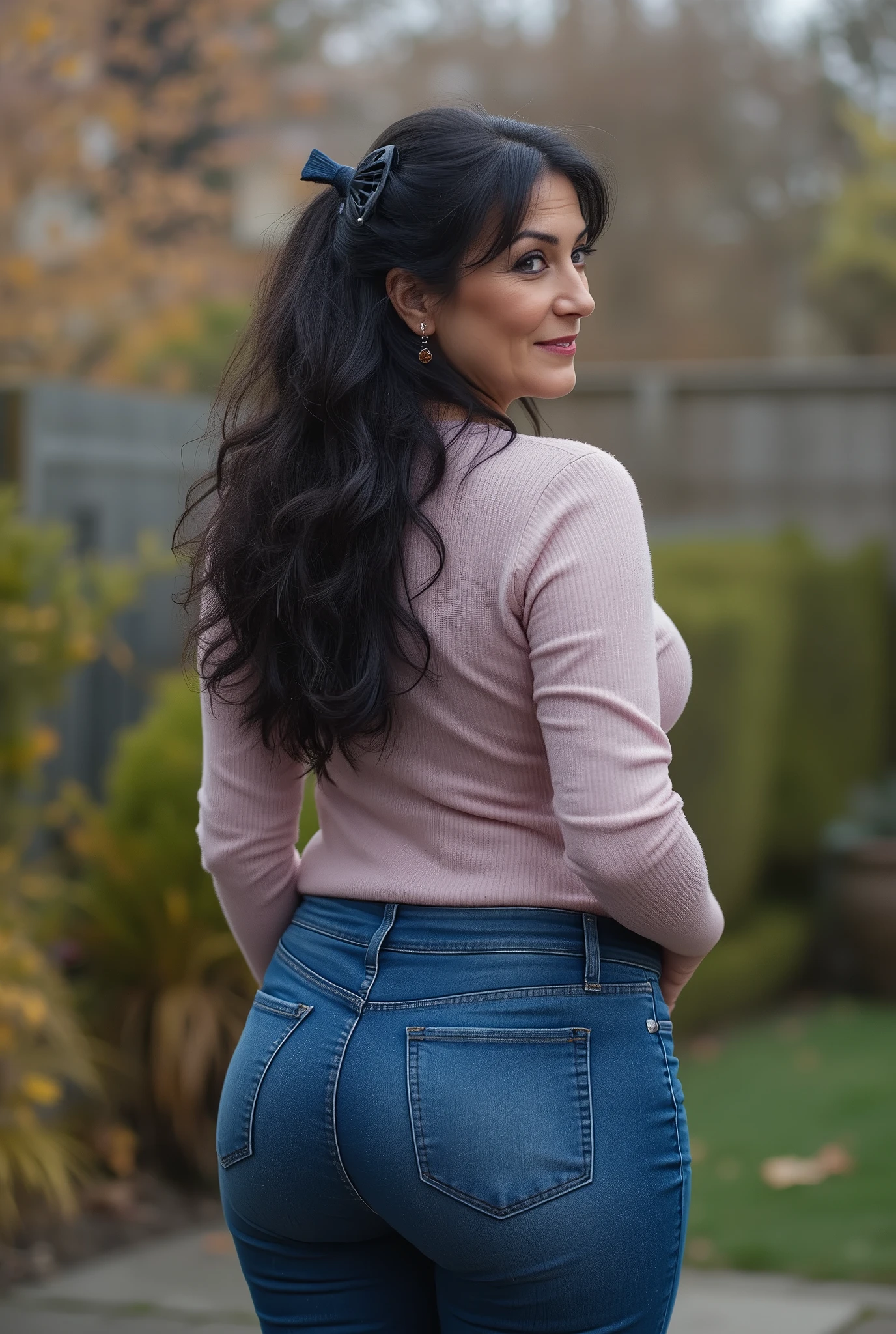 hyperrealistic full-body true rear portrait of mature European woman with unmistakable mom presence captured directly from behind with perfect vertical alignment, long dark wavy hair with natural texture variation loosely gathered and secured with dark blue plastic claw clip allowing elegant tendrils to escape framing neck area, head turned precisely at 45-degree angle over right shoulder revealing partial profile with graceful mature beauty showing refined features and subtle signs of aging adding character, wearing ultra-skinny dark blue jeans with exceptional second-skin fit containing high elastane percentage creating perfect fabric tension across wide pear-shaped buttocks with characteristic pocket placement highlighting wide hip structure contrasting dramatically with notably slim waist, pronounced hourglass body shape with significant proportional difference between hip and waist measurements creating classical feminine silhouette, pale pastel rose form-fitting knit sweater with authentic textile weave showing subtle ribbing pattern at cuffs and hemline, deliberately tucked slightly into waistband at back creating emphasis on waistline and enhancing natural curves, standing with weight slightly shifted to one leg creating subtle natural asymmetry in quiet secluded backyard area with minimal landscaping elements, soft blurred background with muted autumn foliage creating professional bokeh effect enhancing subject isolation, captured in diffused overcast autumn daylight creating even illumination with subtle directional quality, cinematic ultra-detailed 8k photography style with perfect technical execution