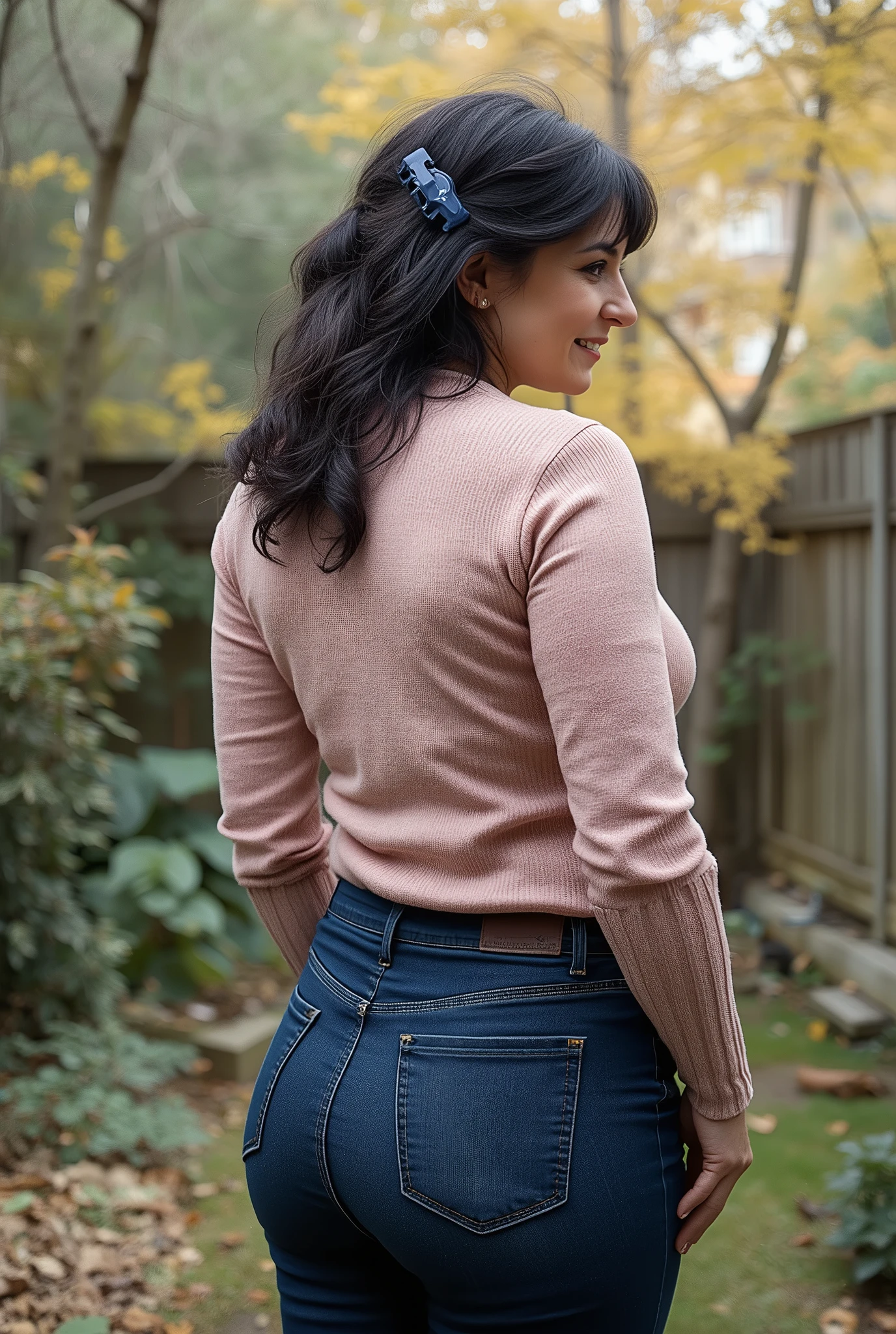 hyperrealistic full-body true rear portrait of mature European woman with unmistakable mom presence captured directly from behind with perfect vertical alignment, long dark wavy hair with natural texture variation loosely gathered and secured with dark blue plastic claw clip allowing elegant tendrils to escape framing neck area, head turned precisely at 45-degree angle over right shoulder revealing partial profile with graceful mature beauty showing refined features and subtle signs of aging adding character, wearing ultra-skinny dark blue jeans with exceptional second-skin fit containing high elastane percentage creating perfect fabric tension across wide pear-shaped buttocks with characteristic pocket placement highlighting wide hip structure contrasting dramatically with notably slim waist, pronounced hourglass body shape with significant proportional difference between hip and waist measurements creating classical feminine silhouette, pale pastel rose form-fitting knit sweater with authentic textile weave showing subtle ribbing pattern at cuffs and hemline, deliberately tucked slightly into waistband at back creating emphasis on waistline and enhancing natural curves, standing with weight slightly shifted to one leg creating subtle natural asymmetry in quiet secluded backyard area with minimal landscaping elements, soft blurred background with muted autumn foliage creating professional bokeh effect enhancing subject isolation, captured in diffused overcast autumn daylight creating even illumination with subtle directional quality, cinematic ultra-detailed 8k photography style with perfect technical execution