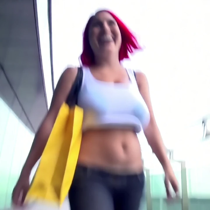 woman with red hair and a white tank top, who is seen in various poses and settings. Initially, she is standing outside a building, smiling and looking at the camera. She then moves to an urban rooftop, where she is seen in a similar pose, looking at the camera. The scene changes to a close-up of her bare breasts, with a focus on her natural beauty. The video then shows her in a different setting, with a yellow bag in her hand, and she is seen in a similar pose as before. Finally, the video ends with a close-up of her bare breasts, with a focus on her natural beauty.