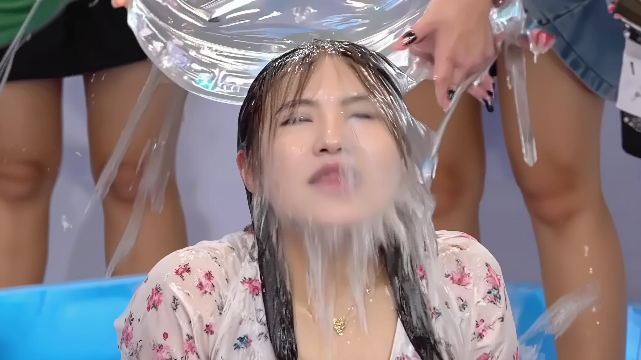 Beautiful young 18-year-old model with long pale blonde hair, cream floral dress with puff sleeves, drenched in cascading water, crystalline rivulets streaming down face, false eyelashes and sparkly eyeshadow visible through water streams, glossy lipstick, thin gold necklace, long black press-on nails, thin gold jewellery glinting through water drops, outdoor lighting, carnival setting, photorealistic portrait, close-up, dramatic water splash captured in motion, high-speed photography