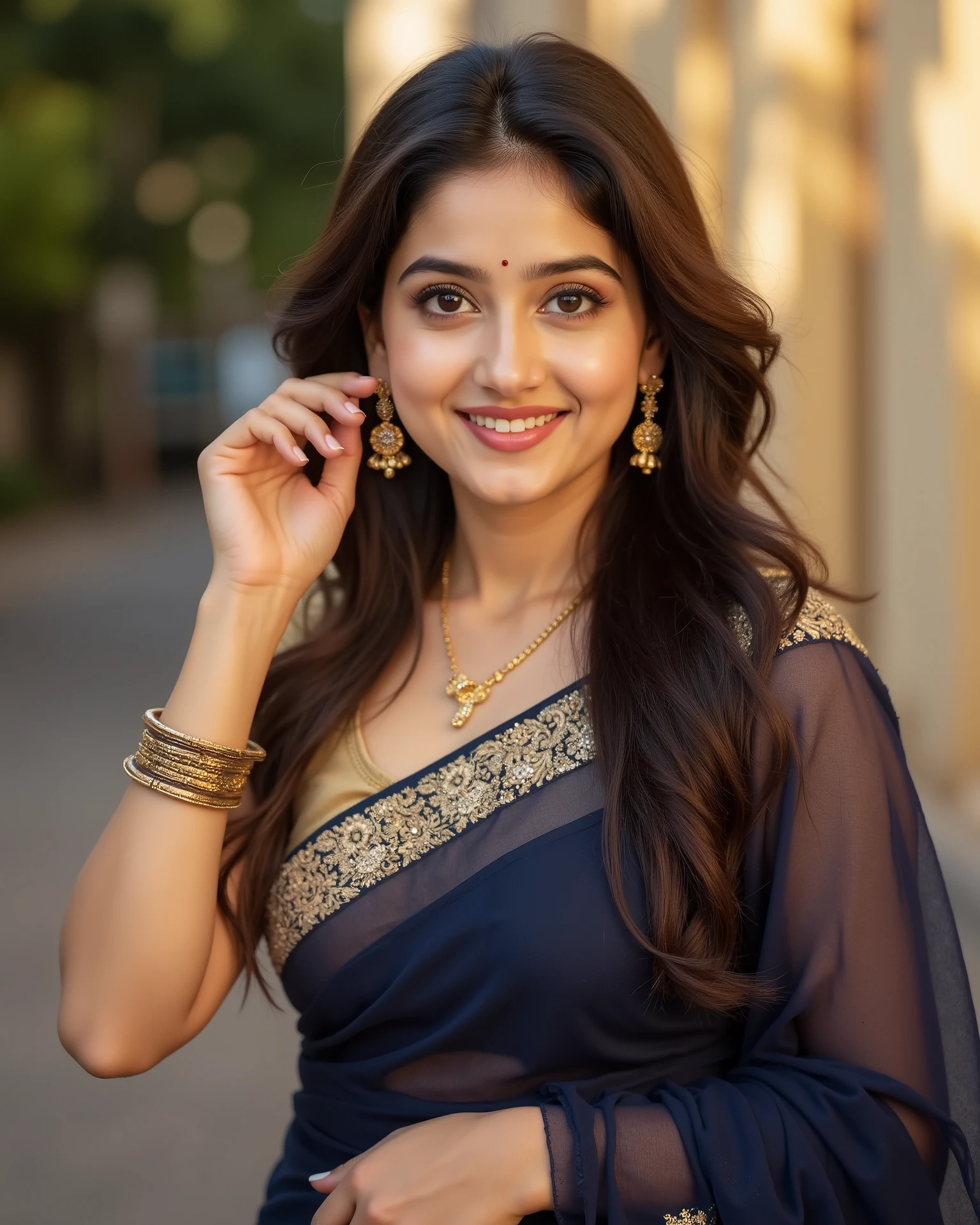 anaswarasdxl, Full body image of a 20 year old Indian girl with smiling look, fair skin tone, light grey eyes, fox eyelashes, thin eyebrows, black eye liner, silver eyeshadow, natural blush, and red lipstick. Her hairs are long, brown, wavy and stylish. She is wearing a navy-blue saree with a golden blouse with thin strap. The jewelry include a golden earrings, a golden necklace and bangles. She is gently adjusting one earring with her right hand while holding the saree with the left hand. The background is softly blurred with warm sunlight. The style is realistic, elegant, and cinematic, with soft lighting and sharp focus on her face and outfit.