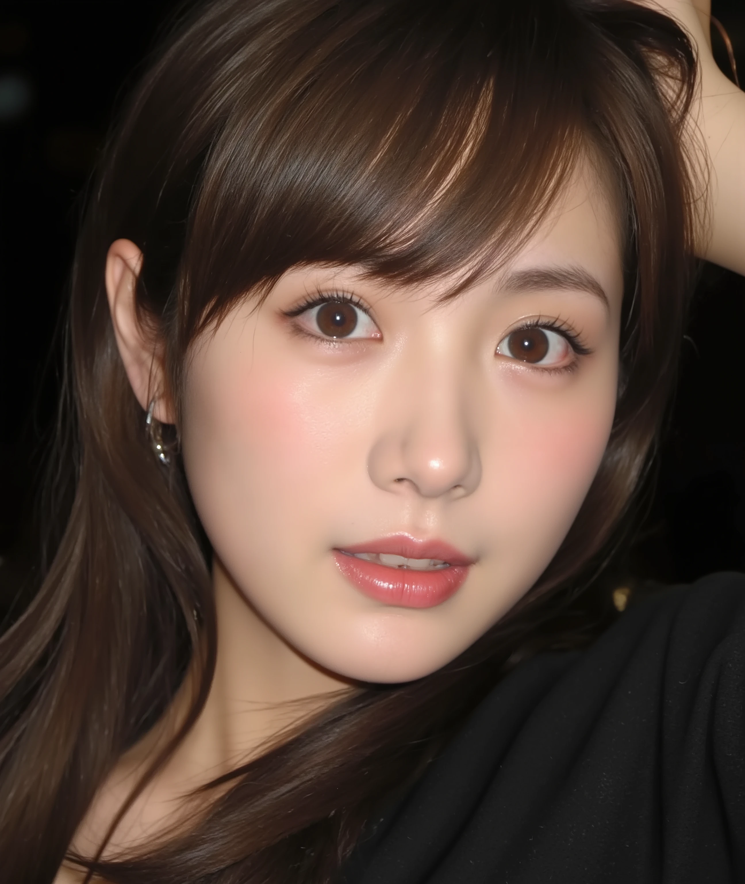 The image is a close-up photograph of a young Asian woman with a fair complexion. Her face dominates the frame, occupying the majority of the image, with her eyes, nose, and lips prominently visible. She has large, almond-shaped eyes with long, thick eyelashes, and her skin is smooth and soft. Her lips are full and slightly parted, revealing a natural, rosy hue. She wears a small silver stud earring in her left ear, adding a subtle touch of personal style.
Her hair is long, dark brown with subtle highlights, and it partially covers her forehead, giving a slightly tousled, casual look. The background is out of focus, but it appears to be a dark, possibly indoor setting, which emphasizes her face and provides a stark contrast to her light complexion. She is wearing a black garment, possibly a top or a sleeve, which is visible at the bottom of the image. The overall mood of the photograph is intimate and personal, capturing a candid moment with a natural, unfiltered aesthetic.