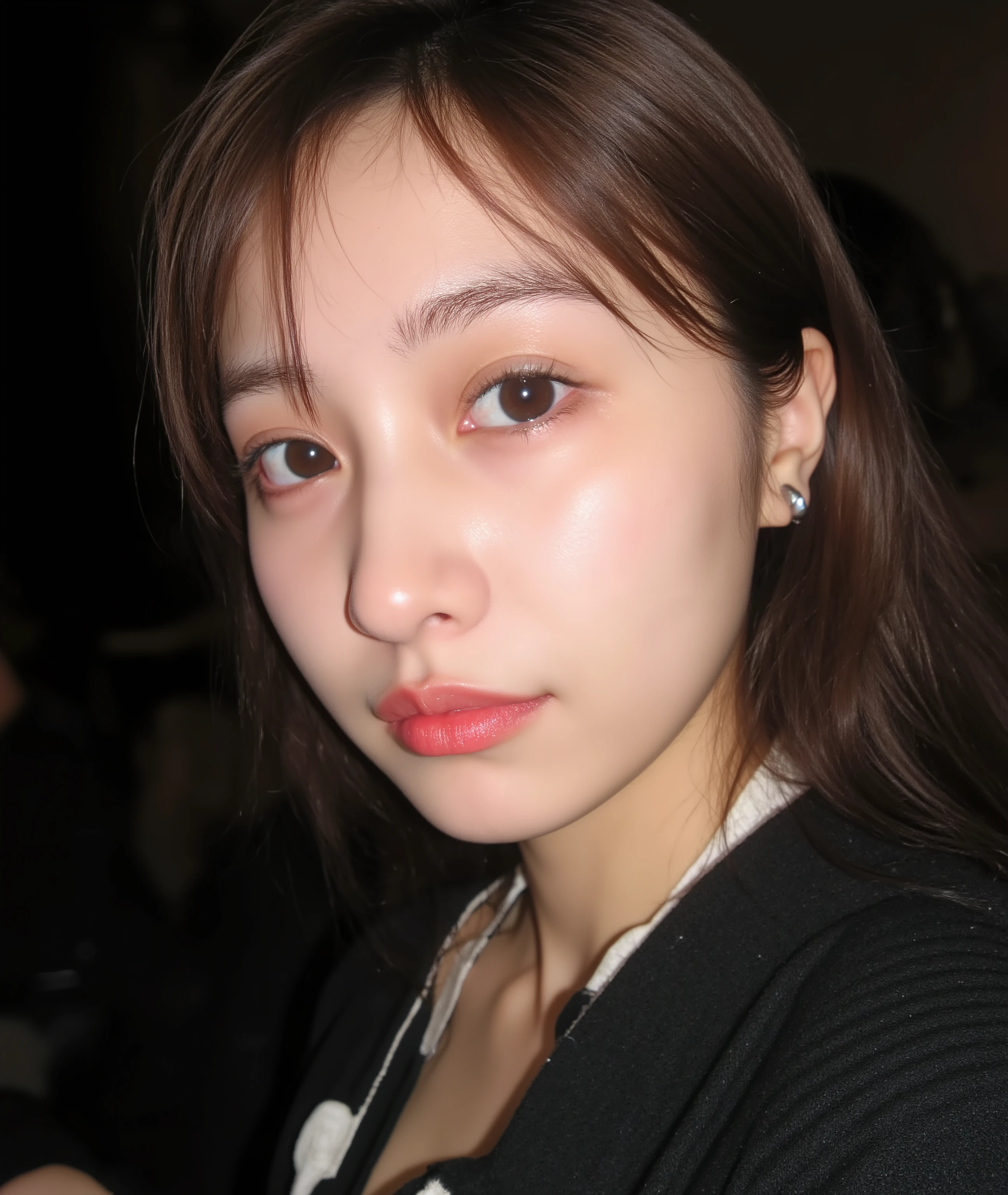 The image is a close-up photograph of a young Asian woman with a fair complexion. Her face dominates the frame, occupying the majority of the image, with her eyes, nose, and lips prominently visible. She has large, almond-shaped eyes with long, thick eyelashes, and her skin is smooth and soft. Her lips are full and slightly parted, revealing a natural, rosy hue. She wears a small silver stud earring in her left ear, adding a subtle touch of personal style.
Her hair is long, dark brown with subtle highlights, and it partially covers her forehead, giving a slightly tousled, casual look. The background is out of focus, but it appears to be a dark, possibly indoor setting, which emphasizes her face and provides a stark contrast to her light complexion. She is wearing a black garment, possibly a top or a sleeve, which is visible at the bottom of the image. The overall mood of the photograph is intimate and personal, capturing a candid moment with a natural, unfiltered aesthetic.