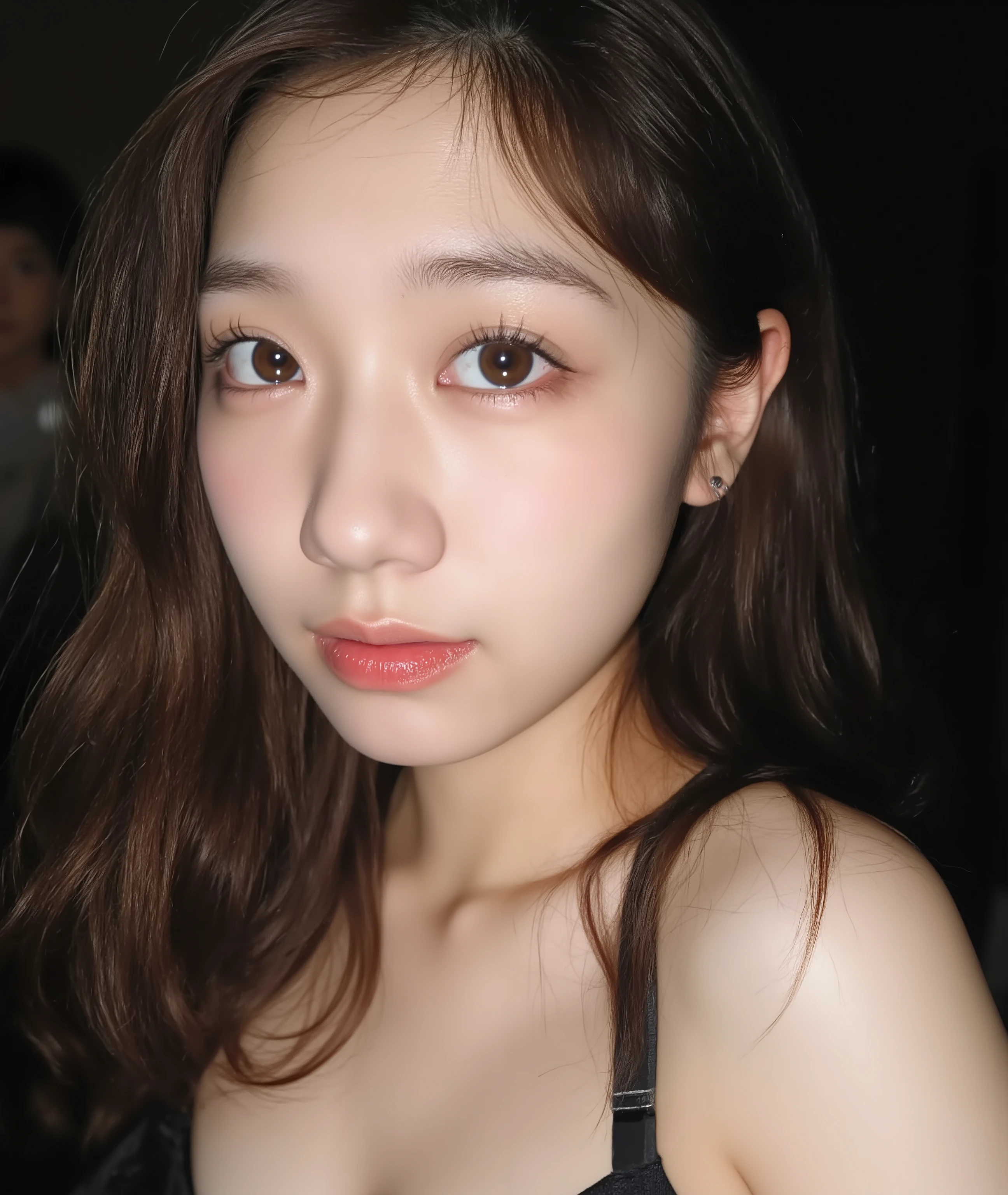 The image is a close-up photograph of a young Asian woman with a fair complexion. Her face dominates the frame, occupying the majority of the image, with her eyes, nose, and lips prominently visible. She has large, almond-shaped eyes with long, thick eyelashes, and her skin is smooth and soft. Her lips are full and slightly parted, revealing a natural, rosy hue. She wears a small silver stud earring in her left ear, adding a subtle touch of personal style.

Her hair is long, dark brown with subtle highlights, and it partially covers her forehead, giving a slightly tousled, casual look. The background is out of focus, but it appears to be a dark, possibly indoor setting, which emphasizes her face and provides a stark contrast to her light complexion. She is wearing a black garment, possibly a top or a sleeve, which is visible at the bottom of the image. The overall mood of the photograph is intimate and personal, capturing a candid moment with a natural, unfiltered aesthetic.