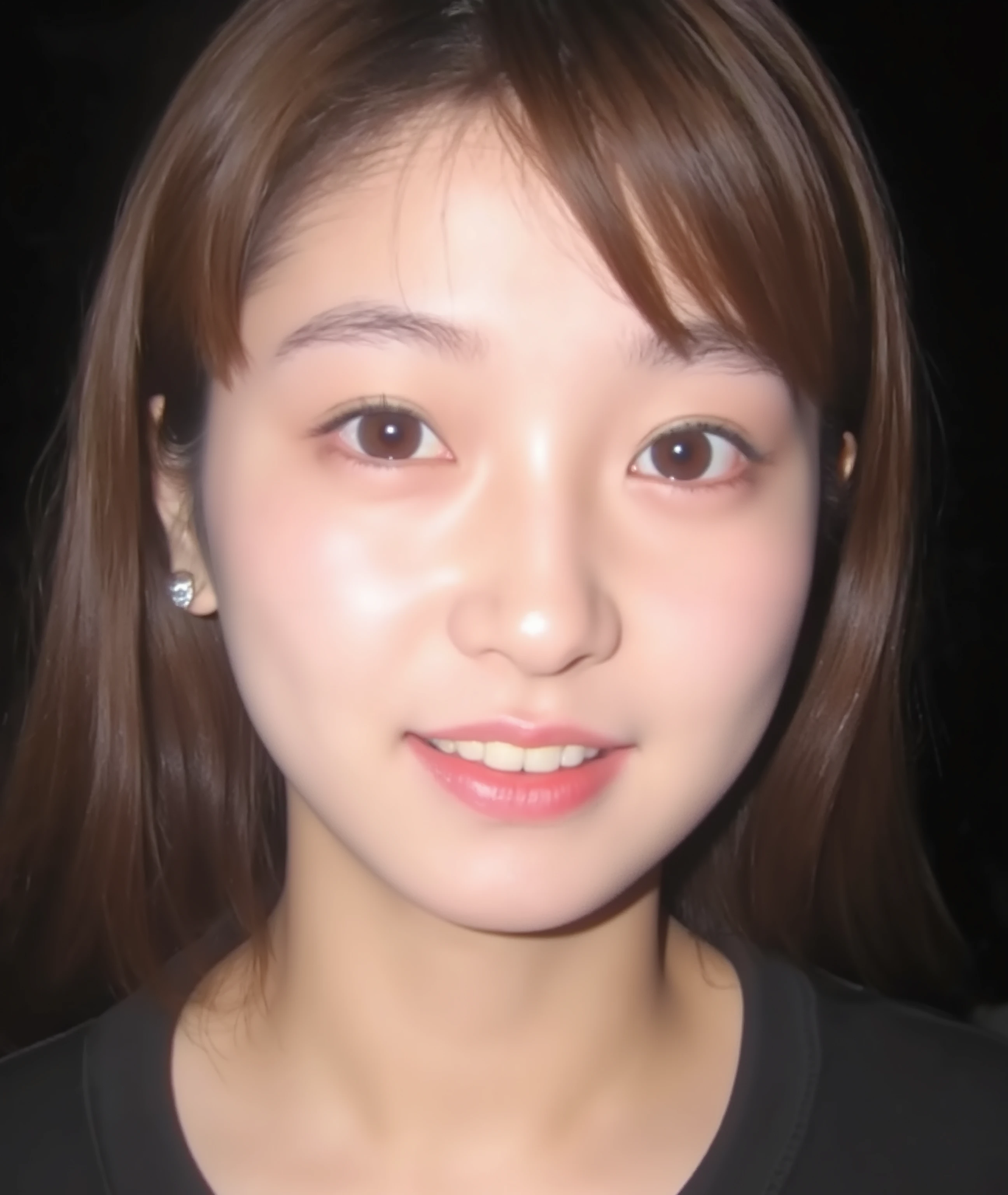 The image is a close-up photograph of a young Asian woman with a fair complexion. Her face dominates the frame, occupying the majority of the image, with her eyes, nose, and lips prominently visible. She has large, almond-shaped eyes with long, thick eyelashes, and her skin is smooth and soft. Her lips are full and slightly parted, revealing a natural, rosy hue. She wears a small silver stud earring in her left ear, adding a subtle touch of personal style.
Her hair is long, dark brown with subtle highlights, and it partially covers her forehead, giving a slightly tousled, casual look. The background is out of focus, but it appears to be a dark, possibly indoor setting, which emphasizes her face and provides a stark contrast to her light complexion. She is wearing a black garment, possibly a top or a sleeve, which is visible at the bottom of the image. The overall mood of the photograph is intimate and personal, capturing a candid moment with a natural, unfiltered aesthetic.