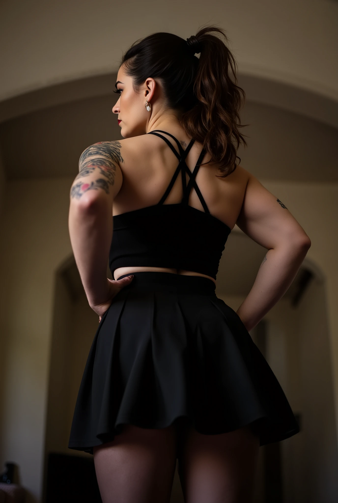 imposing rear-angle portrait of domineering European woman with stout powerful build, wide hips and thick strong legs in authoritative stance, minimal head turn revealing just a glimpse of stern profile with intense sidelong glare, wavy dark brown hair tied into full long ponytail, fitted black pleated skirt with sheer black tights showcasing her substantial curves, black tank top with straps crossing her broad back, tattoos on arms, back deliberately arched to assert dominance while emphasizing her full rounded buttocks, shot from extremely low submissive angle with ceiling visible beyond her towering form, bright daylight creating dramatic shadows that accentuate her commanding presence, photorealistic, high definition, studio lighting, cinematic composition, dramatic shadows