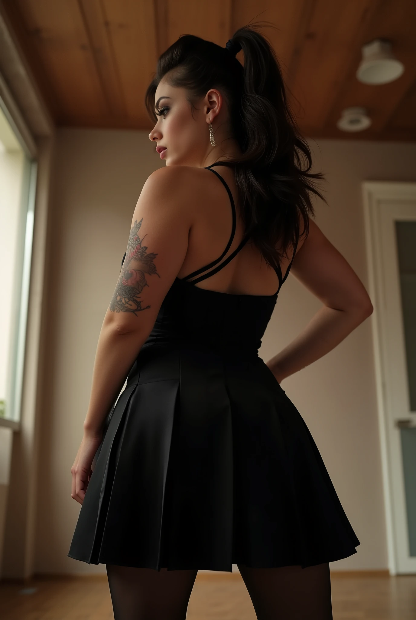 imposing rear-angle portrait of domineering European woman with stout powerful build, wide hips and thick strong legs in authoritative stance, minimal head turn revealing just a glimpse of stern profile with intense sidelong glare, wavy dark brown hair inspired by rockabilly style and tied into long full ponytail, fitted black pleated skirt with sheer black tights showcasing her substantial curves, black tank top with thin straps along her broad back, small tattoos on arms, back deliberately arched to assert dominance while emphasizing her full rounded buttocks, shot from extremely low submissive angle with ceiling visible beyond her towering form, bright daylight creating dramatic shadows that accentuate her commanding presence