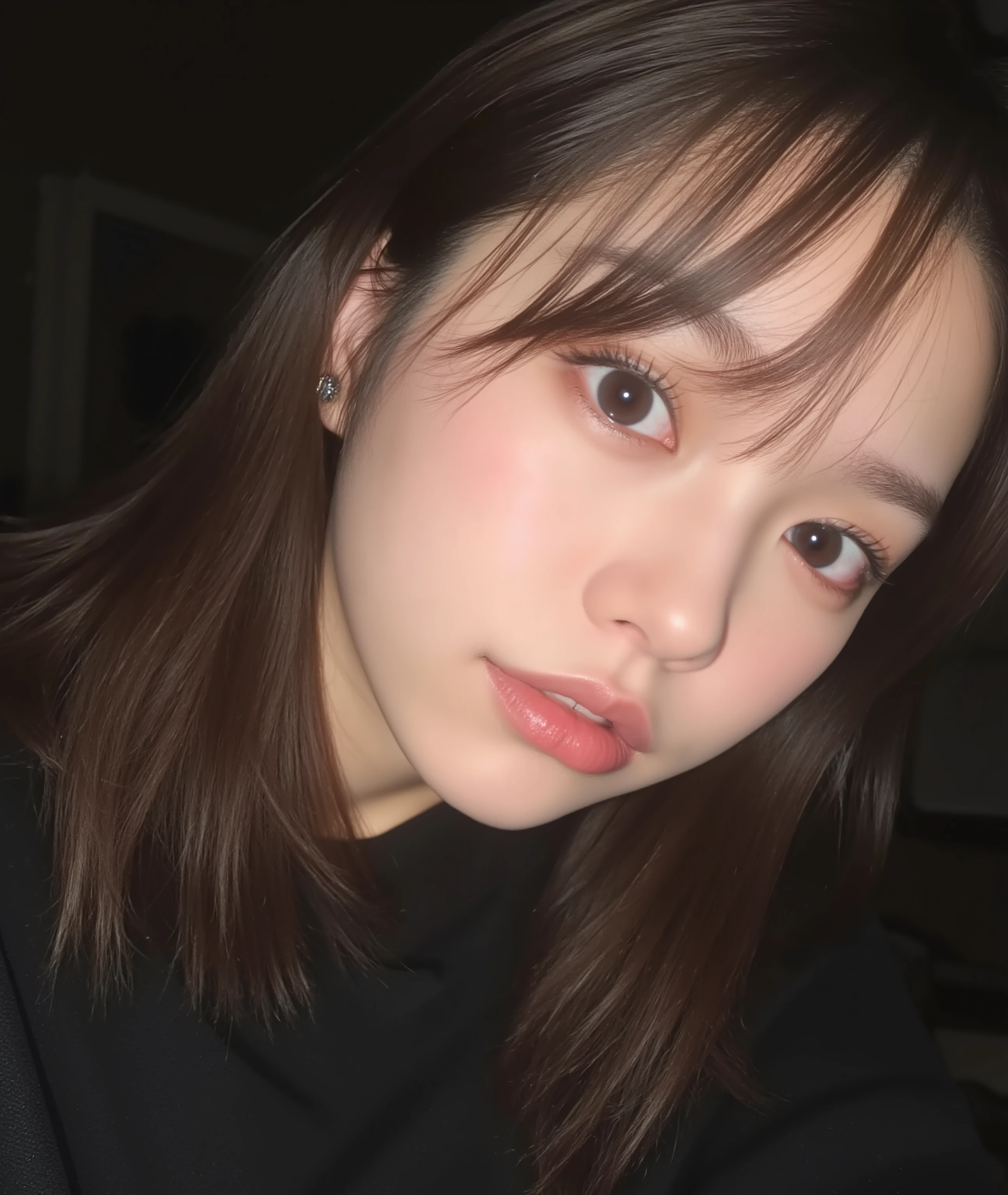 The image is a close-up photograph of a young Asian woman with a fair complexion. Her face dominates the frame, occupying the majority of the image, with her eyes, nose, and lips prominently visible. She has large, almond-shaped eyes with long, thick eyelashes, and her skin is smooth and soft. Her lips are full and slightly parted, revealing a natural, rosy hue. She wears a small silver stud earring in her left ear, adding a subtle touch of personal style.

Her hair is long, dark brown with subtle highlights, and it partially covers her forehead, giving a slightly tousled, casual look. The background is out of focus, but it appears to be a dark, possibly indoor setting, which emphasizes her face and provides a stark contrast to her light complexion. She is wearing a black garment, possibly a top or a sleeve, which is visible at the bottom of the image. The overall mood of the photograph is intimate and personal, capturing a candid moment with a natural, unfiltered aesthetic.