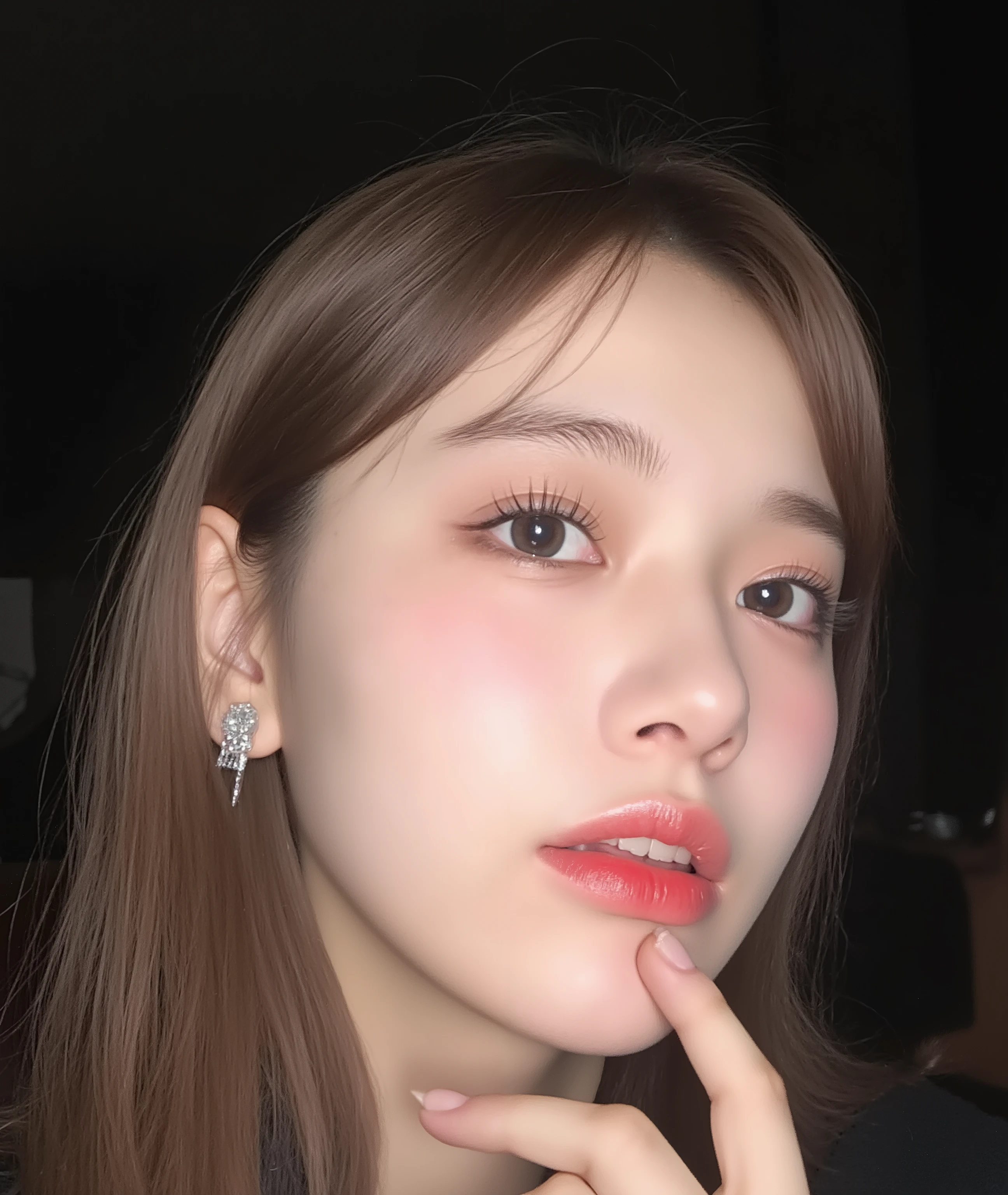 The image is a close-up photograph of a young Asian woman with a fair complexion. Her face dominates the frame, occupying the majority of the image, with her eyes, nose, and lips prominently visible. She has large, almond-shaped eyes with long, thick eyelashes, and her skin is smooth and soft. Her lips are full and slightly parted, revealing a natural, rosy hue. She wears a small silver stud earring in her left ear, adding a subtle touch of personal style.

Her hair is long, dark brown with subtle highlights, and it partially covers her forehead, giving a slightly tousled, casual look. The background is out of focus, but it appears to be a dark, possibly indoor setting, which emphasizes her face and provides a stark contrast to her light complexion. She is wearing a black garment, possibly a top or a sleeve, which is visible at the bottom of the image. The overall mood of the photograph is intimate and personal, capturing a candid moment with a natural, unfiltered aesthetic.