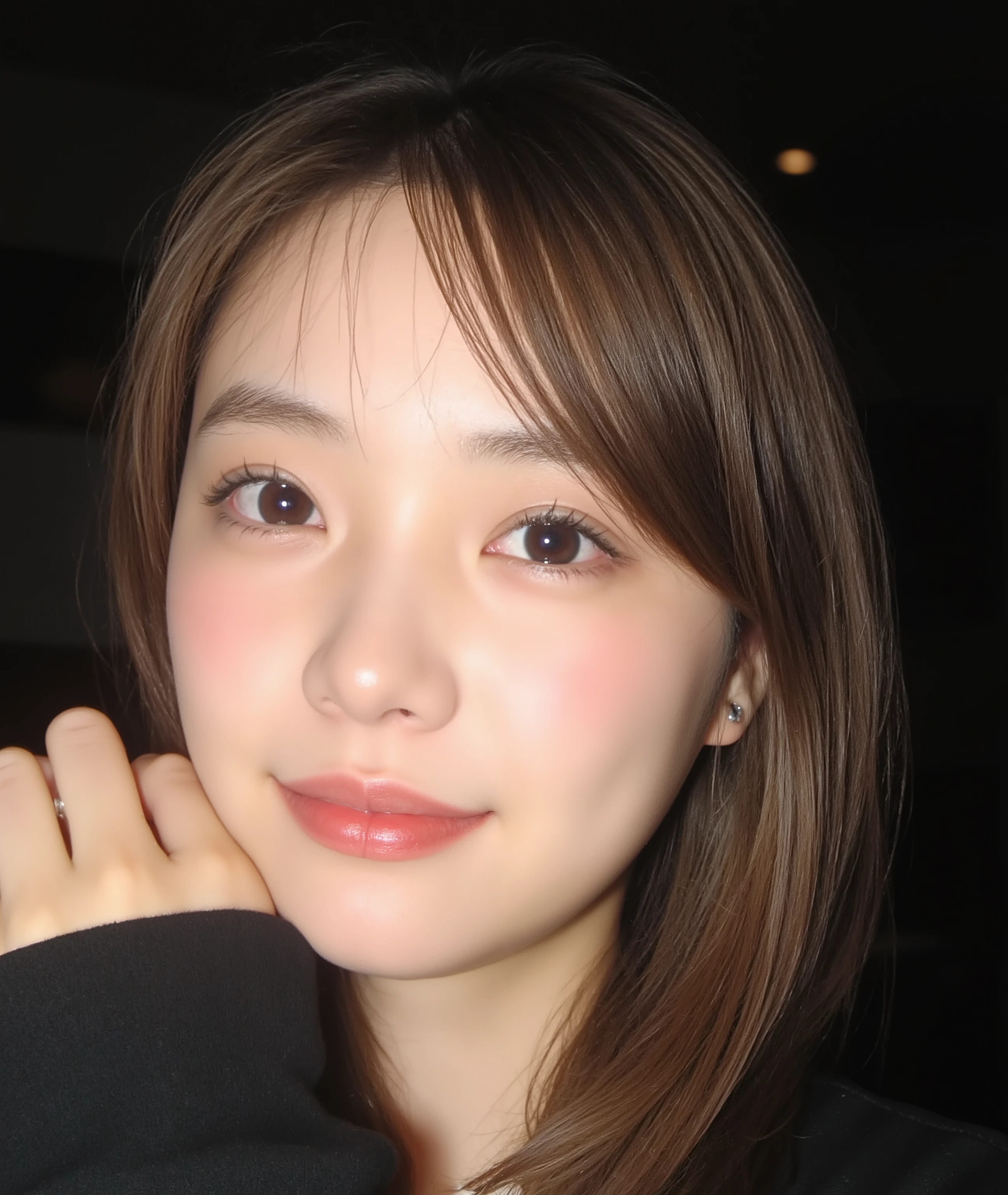 The image is a close-up photograph of a young Asian woman with a fair complexion. Her face dominates the frame, occupying the majority of the image, with her eyes, nose, and lips prominently visible. She has large, almond-shaped eyes with long, thick eyelashes, and her skin is smooth and soft. Her lips are full and slightly parted, revealing a natural, rosy hue. She wears a small silver stud earring in her left ear, adding a subtle touch of personal style.
Her hair is long, dark brown with subtle highlights, and it partially covers her forehead, giving a slightly tousled, casual look. The background is out of focus, but it appears to be a dark, possibly indoor setting, which emphasizes her face and provides a stark contrast to her light complexion. She is wearing a black garment, possibly a top or a sleeve, which is visible at the bottom of the image. The overall mood of the photograph is intimate and personal, capturing a candid moment with a natural, unfiltered aesthetic.