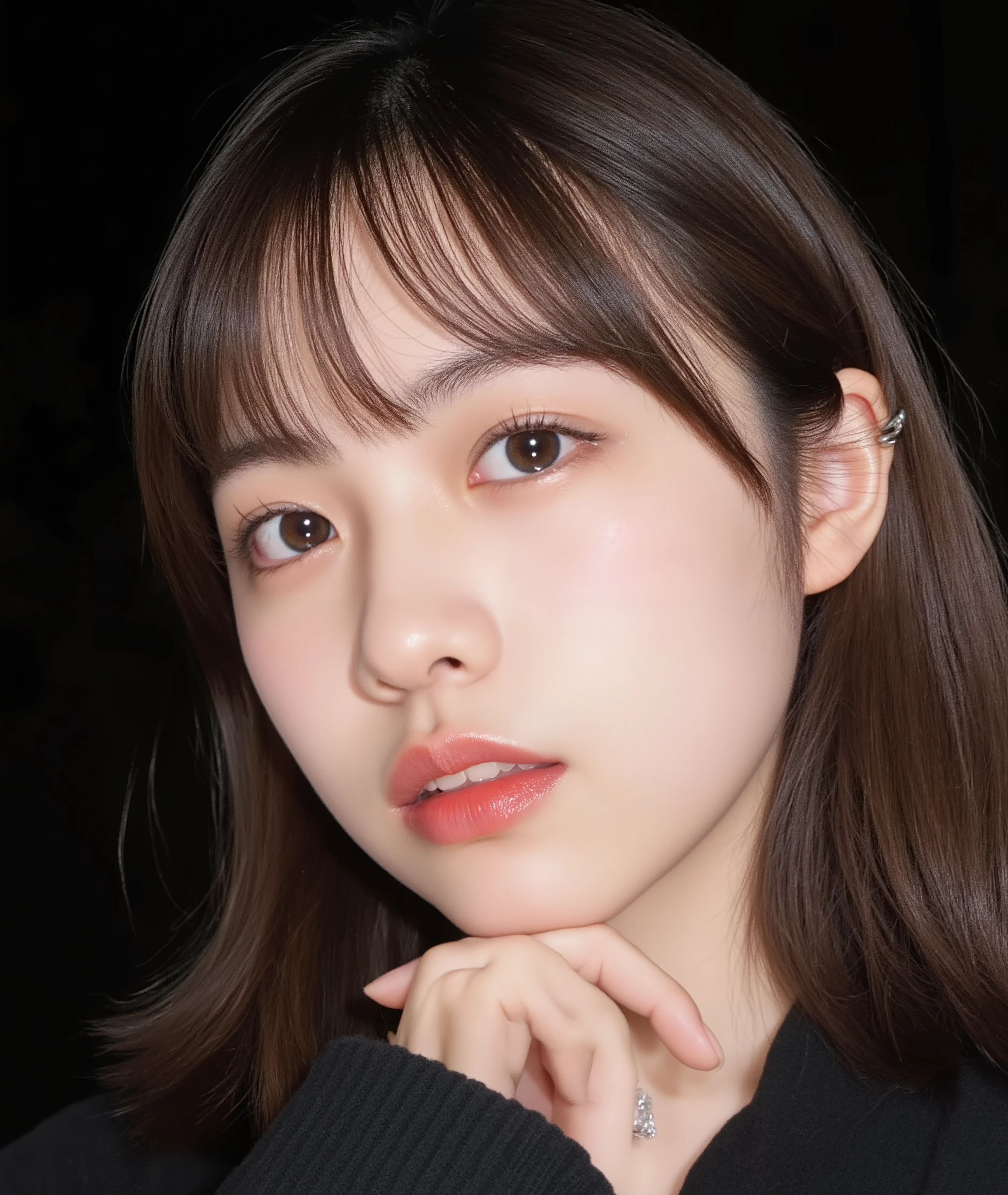 The image is a close-up photograph of a young Asian woman with a fair complexion. Her face dominates the frame, occupying the majority of the image, with her eyes, nose, and lips prominently visible. She has large, almond-shaped eyes with long, thick eyelashes, and her skin is smooth and soft. Her lips are full and slightly parted, revealing a natural, rosy hue. She wears a small silver stud earring in her left ear, adding a subtle touch of personal style.
Her hair is long, dark brown with subtle highlights, and it partially covers her forehead, giving a slightly tousled, casual look. The background is out of focus, but it appears to be a dark, possibly indoor setting, which emphasizes her face and provides a stark contrast to her light complexion. She is wearing a black garment, possibly a top or a sleeve, which is visible at the bottom of the image. The overall mood of the photograph is intimate and personal, capturing a candid moment with a natural, unfiltered aesthetic.