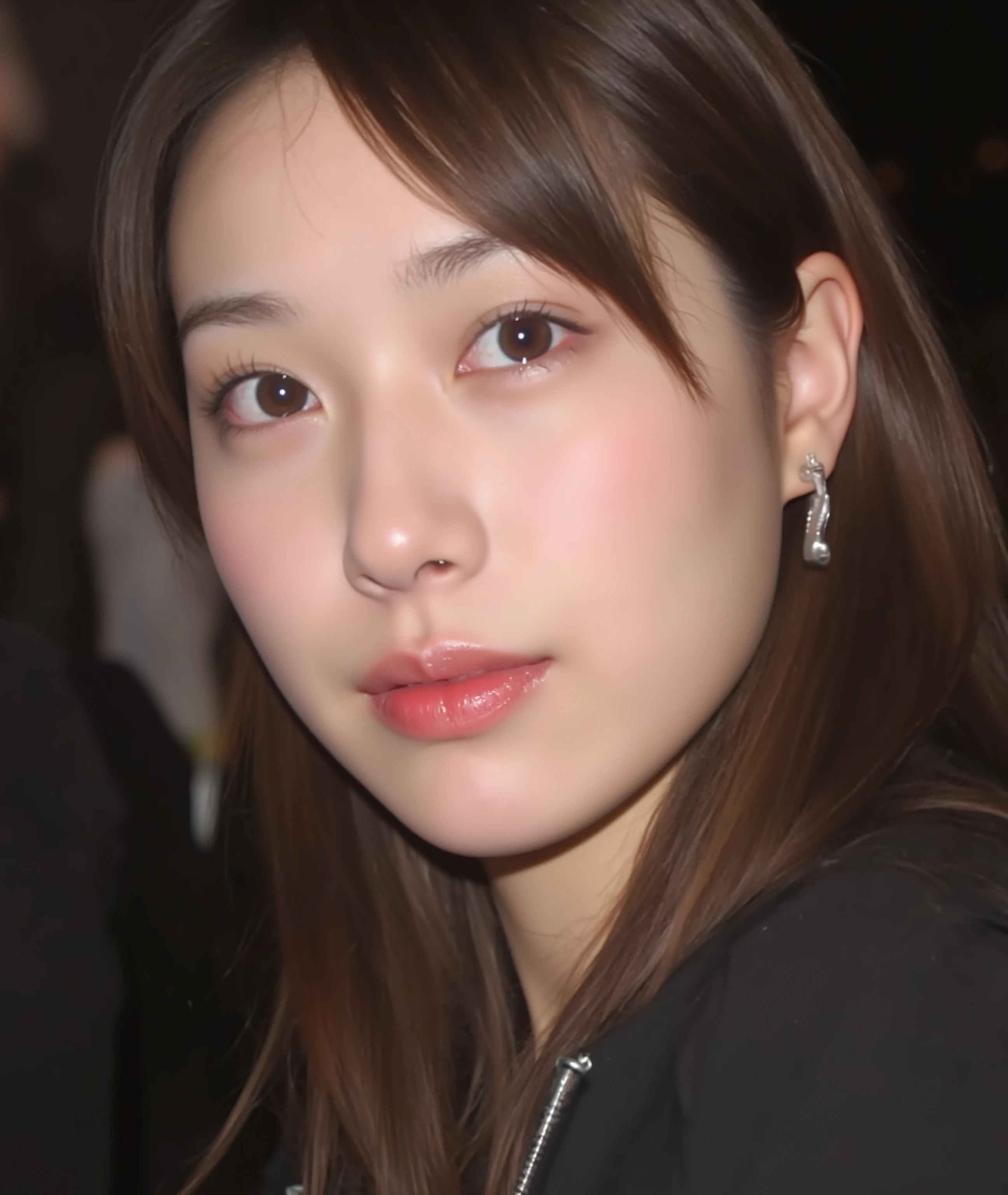 The image is a close-up photograph of a young Asian woman with a fair complexion. Her face dominates the frame, occupying the majority of the image, with her eyes, nose, and lips prominently visible. She has large, almond-shaped eyes with long, thick eyelashes, and her skin is smooth and soft. Her lips are full and slightly parted, revealing a natural, rosy hue. She wears a small silver stud earring in her left ear, adding a subtle touch of personal style.
Her hair is long, dark brown with subtle highlights, and it partially covers her forehead, giving a slightly tousled, casual look. The background is out of focus, but it appears to be a dark, possibly indoor setting, which emphasizes her face and provides a stark contrast to her light complexion. She is wearing a black garment, possibly a top or a sleeve, which is visible at the bottom of the image. The overall mood of the photograph is intimate and personal, capturing a candid moment with a natural, unfiltered aesthetic.