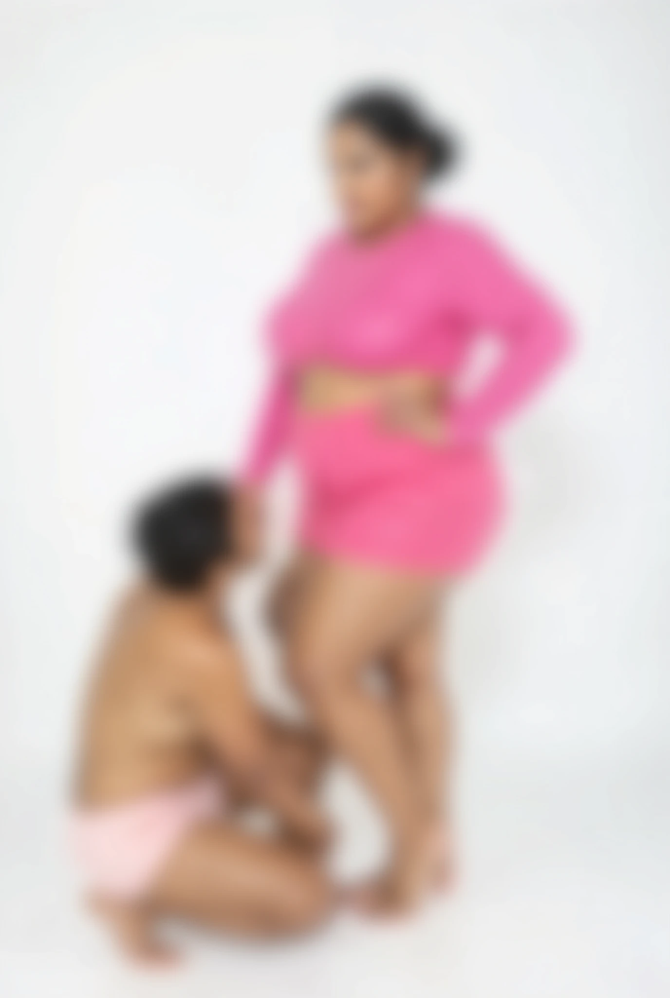 Busty mature ramya krishnan,thick thighs, and big breasts ,hair in tied up hair bun, white skin wearing  plus size long sleeve pink high neac crop top and plus size pink mini short  posing confidently in front of camera barefoot, in white background ,one 20yerars man kneeled down rubbed her shorts, he wearing only panties ,this image was realistic natural ,ultra realistic high quality of 4k image 