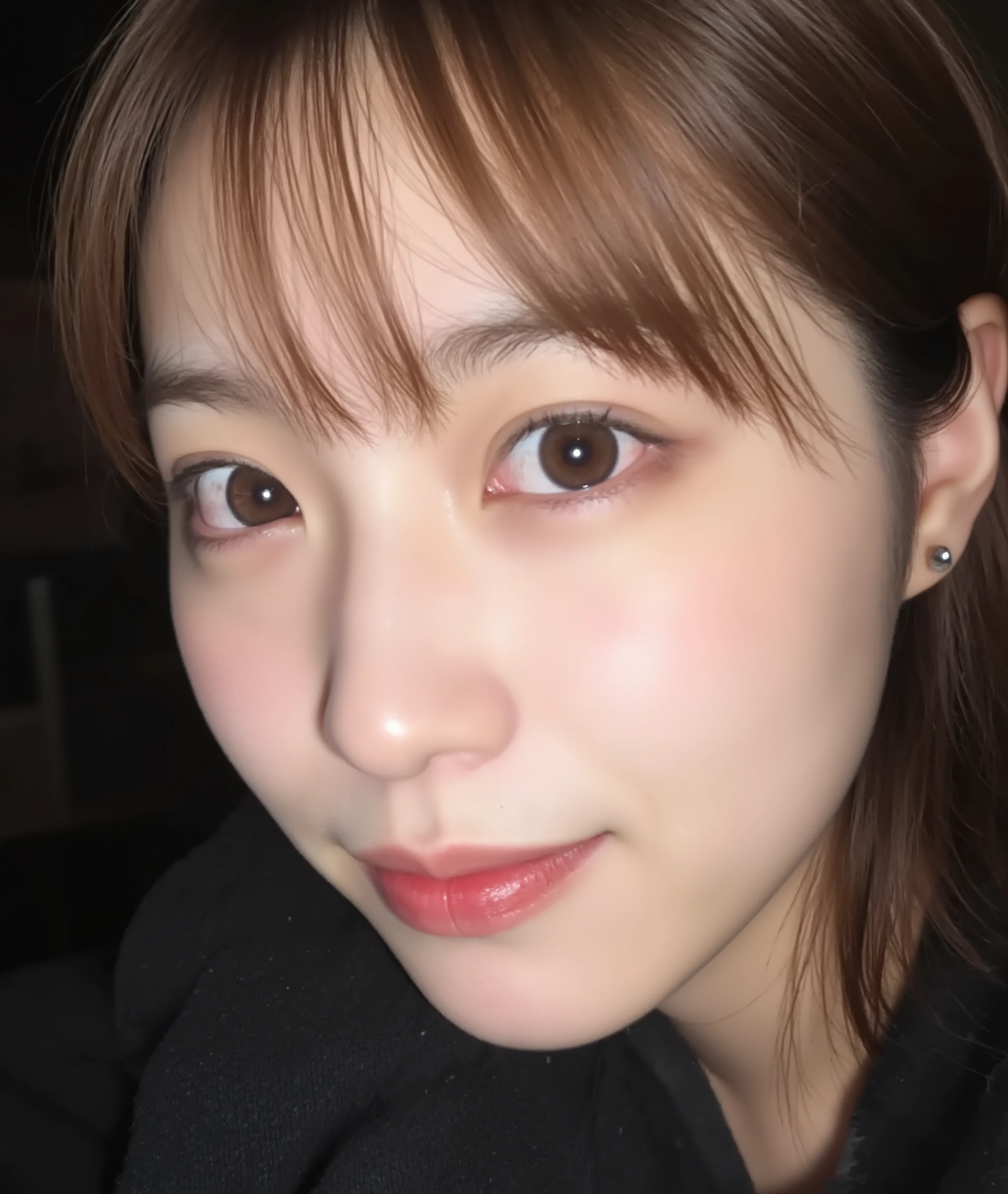 The image is a close-up photograph of a young Asian woman with a fair complexion. Her face dominates the frame, occupying the majority of the image, with her eyes, nose, and lips prominently visible. She has large, almond-shaped eyes with long, thick eyelashes, and her skin is smooth and soft. Her lips are full and slightly parted, revealing a natural, rosy hue. She wears a small silver stud earring in her left ear, adding a subtle touch of personal style.
Her hair is long, dark brown with subtle highlights, and it partially covers her forehead, giving a slightly tousled, casual look. The background is out of focus, but it appears to be a dark, possibly indoor setting, which emphasizes her face and provides a stark contrast to her light complexion. She is wearing a black garment, possibly a top or a sleeve, which is visible at the bottom of the image. The overall mood of the photograph is intimate and personal, capturing a candid moment with a natural, unfiltered aesthetic.