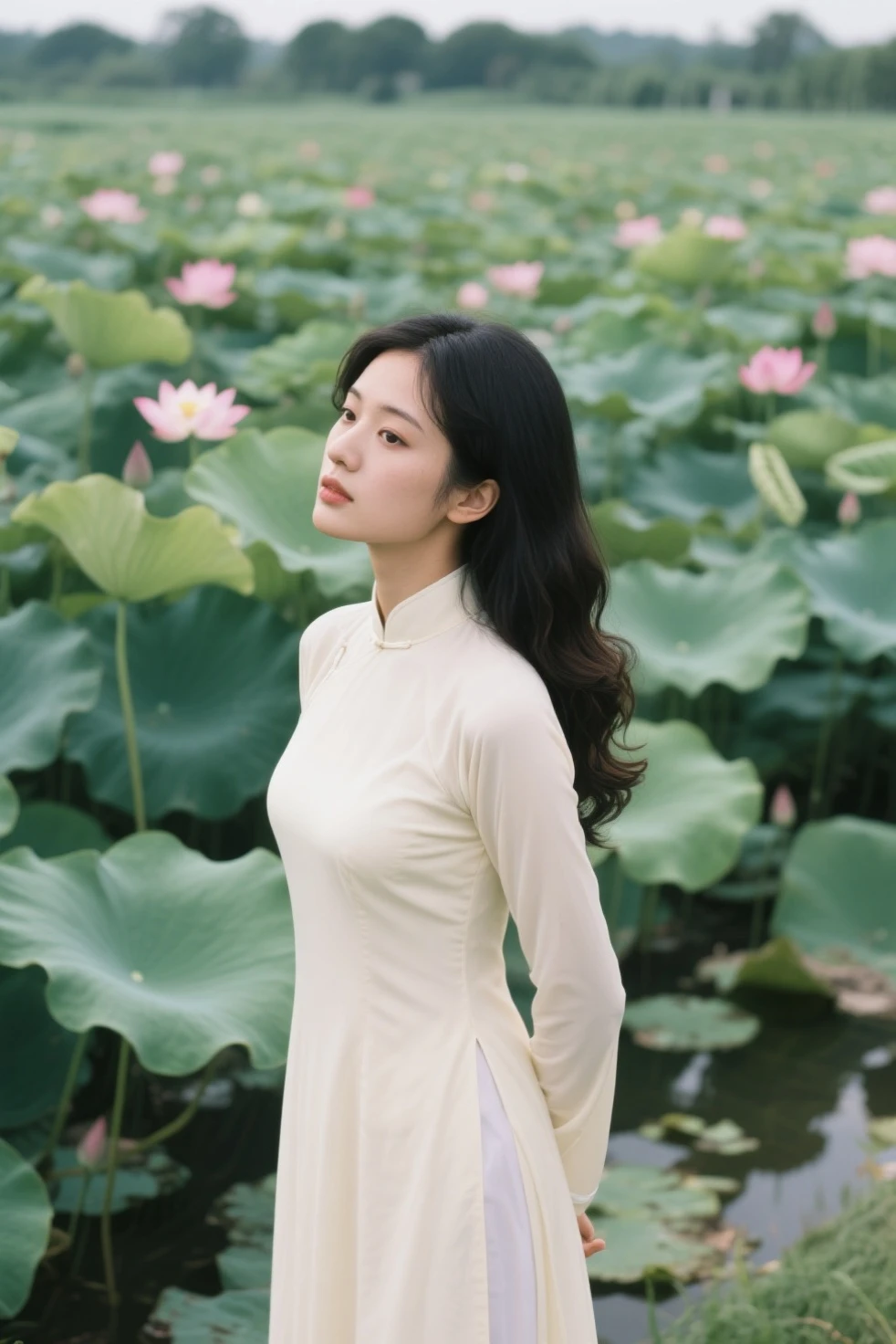 A full-body portrait of a beautiful young woman with long black hair, sitting gracefully among pink lotus flowers. She is wearing a traditional white "ao dai" dress, detailed with lace and delicate embroidery. The background is softly lit with shades of green and pink, complementing the natural beauty of the lotus flowers. The woman is looking down gently, holding a lotus bud in her hands, and her expression reflects calmness and serenity. The overall scene exudes elegance and tranquility, with the pink lotus flowers and green leaves creating a harmonious and serene atmosphere.