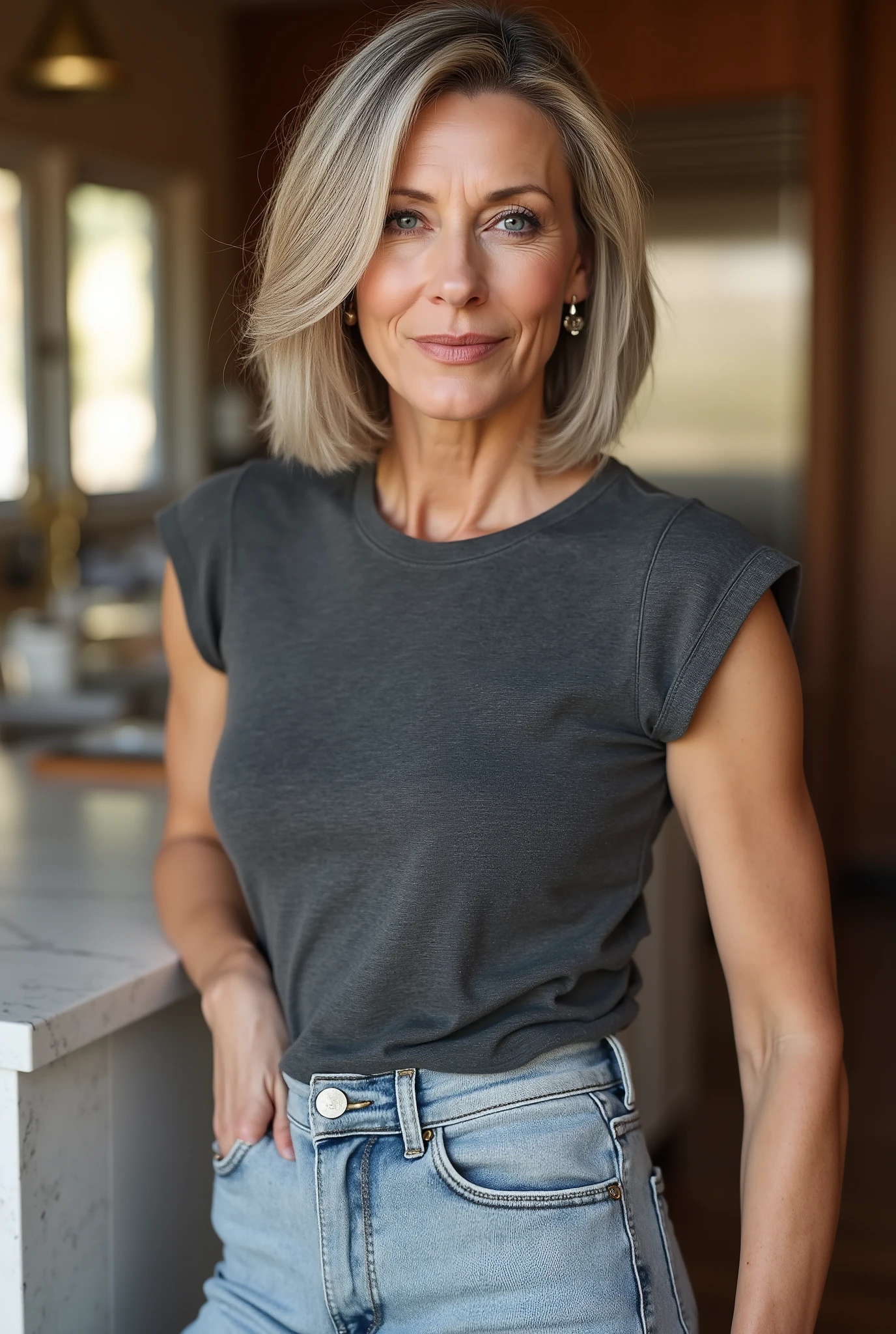 Commanding lifestyle portrait of a 60-year-old woman embracing youthful fashion with champagne grey blunt cut bob and deep side-swept bangs partially covering one eye, thin face with expressive blue eyes showing depth and character, natural aging with distinguished crow's feet, wearing an age-defying fitted faded dark grey t-shirt with cap sleeves, tucked neatly into light-washed skinny tight flared jeans that accentuate her figure, black boots completing the contemporary look, posed confidently against a marble kitchen island with hip slightly cocked, morning sunlight filtering through windows creating dimensional lighting, photorealistic style capturing the bold contrast between her mature features and trendy clothing choices, warm-toned kitchen interior with wooden elements and brass accents, professional photography with shallow depth of field, 85mm lens, f/2.0 aperture